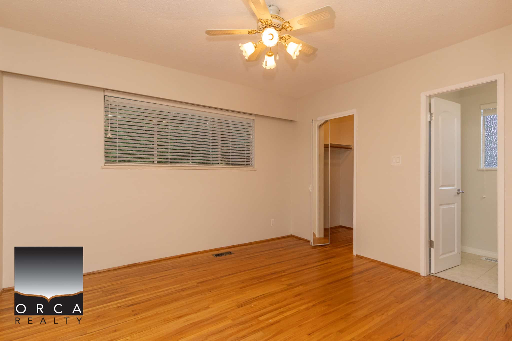 Bright modern bedroom featuring hardwood floors, ceiling fan with lights, spacious closet, and adjacent bathroom with window, perfect for Toronto homebuyers seeking comfort and style.