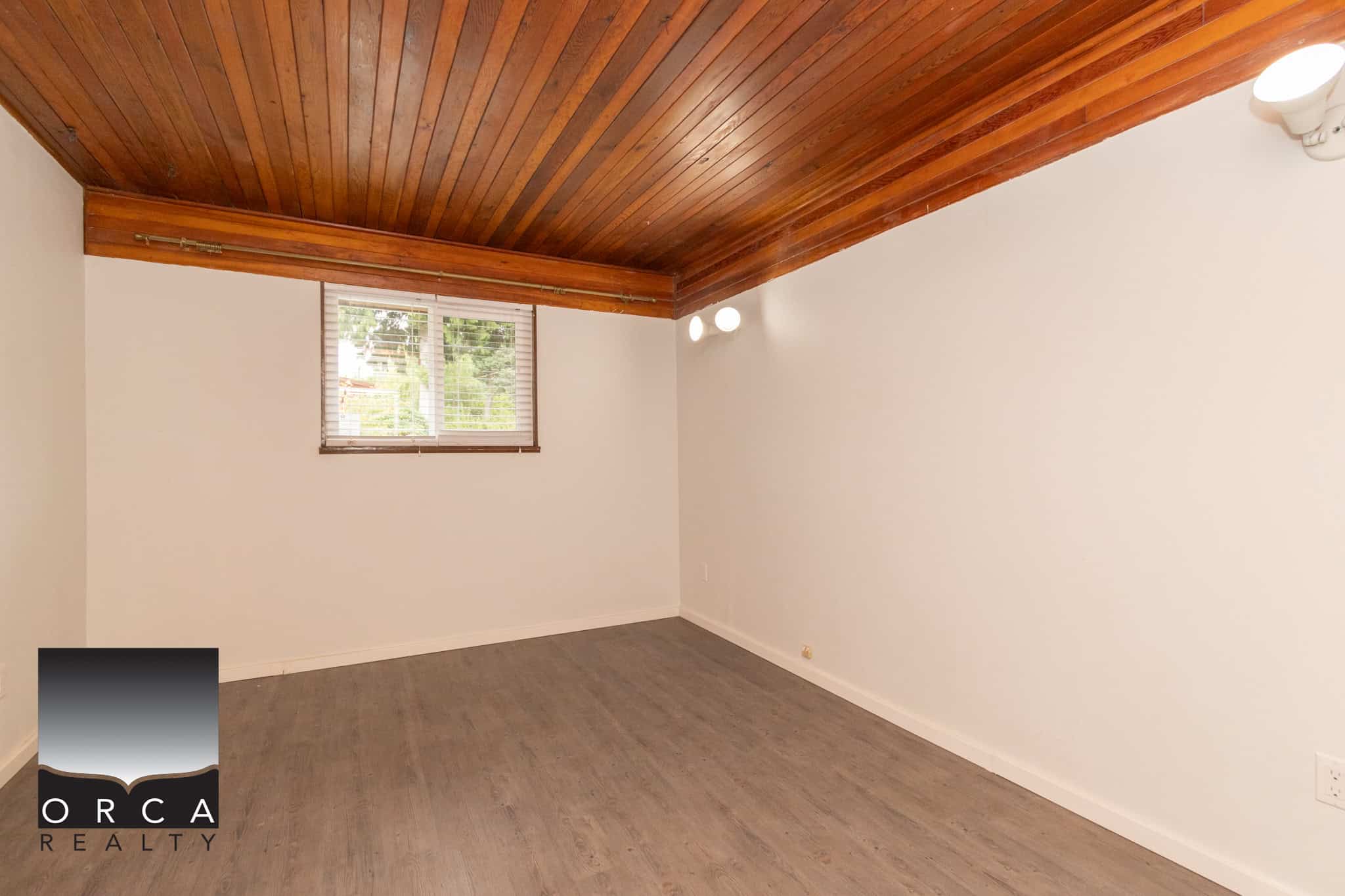 19 Spacious empty room with white walls, wood flooring, and a wooden ceiling in a property listed by Orca Realty Inc., showcasing modern interior design.