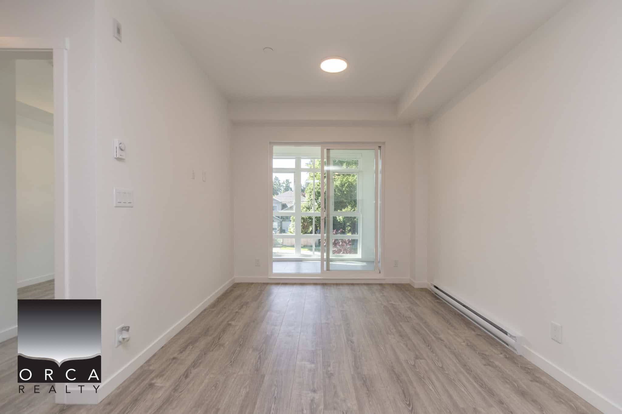 Bright modern living room with large glass door leading to balcony, featuring light wood flooring and white walls, ideal for family gatherings and entertaining.