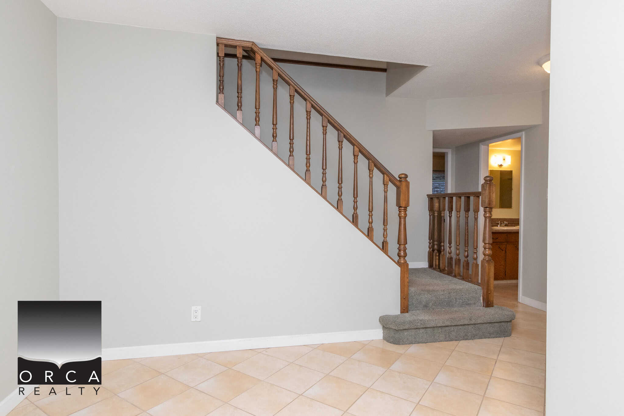 Spacious interior view of a home featuring a wooden staircase with carpeted steps and beige tiled flooring, perfect for showcasing Vancouver Island residential properties.