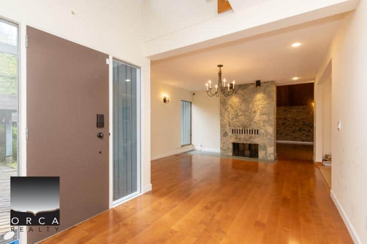 Modern interior of a residential living room with hardwood floors, fireplace, chandelier, and large windows, showcasing available property from Orca Realty Inc. in Vancouver, BC.