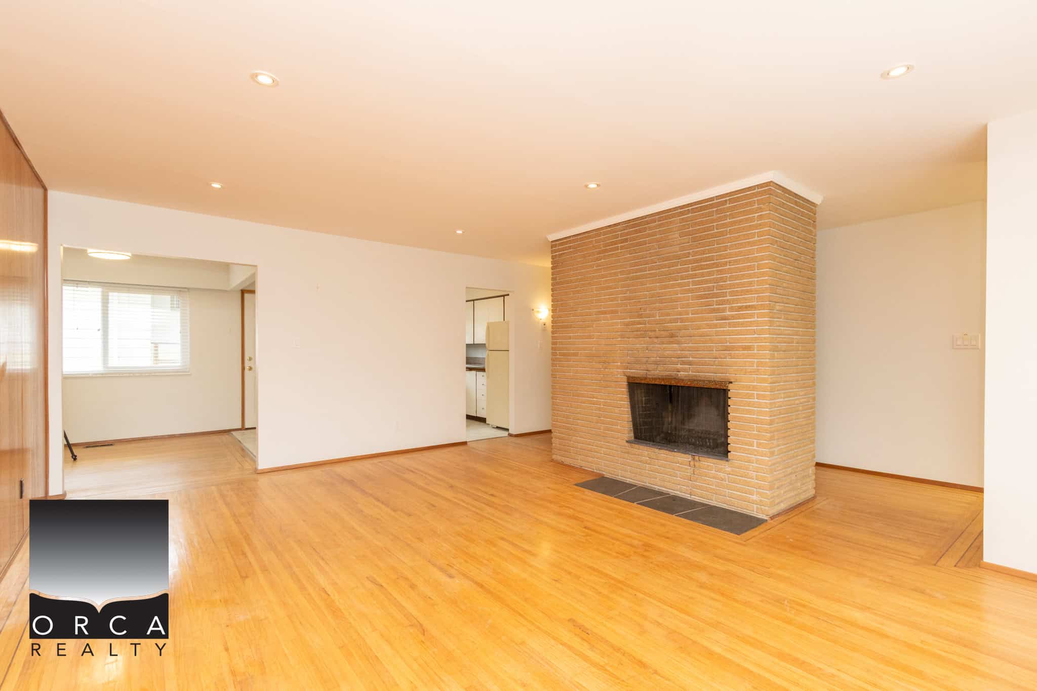 2 Spacious living room with hardwood flooring, brick fireplace, and open layout, ideal for Vancouver Island real estate buyers seeking a cozy home.