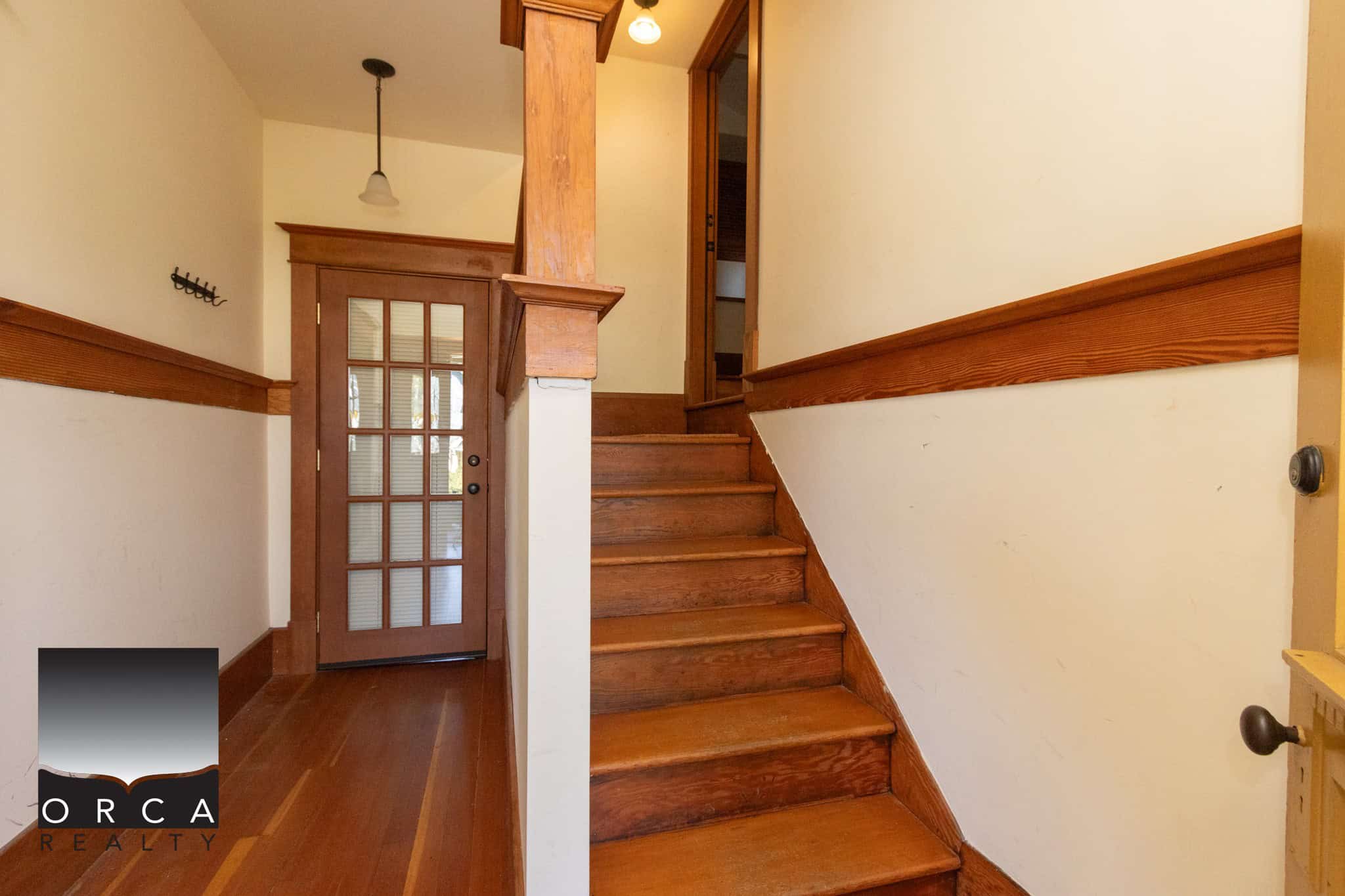 Cozy wooden staircase entrance in a charming home, featuring warm-toned hardwood flooring, classic wooden trim, and a glass-paneled door, perfect for Vancouver Island real estate properties.