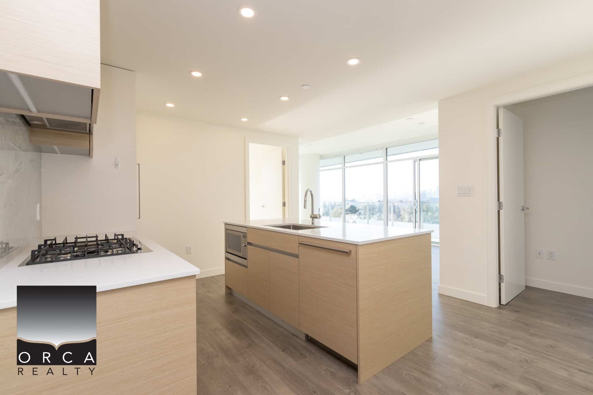 Bright modern kitchen with natural wood cabinets, stainless steel appliances, and panoramic city views from large glass sliding doors. Perfect for contemporary Vancouver real estate.