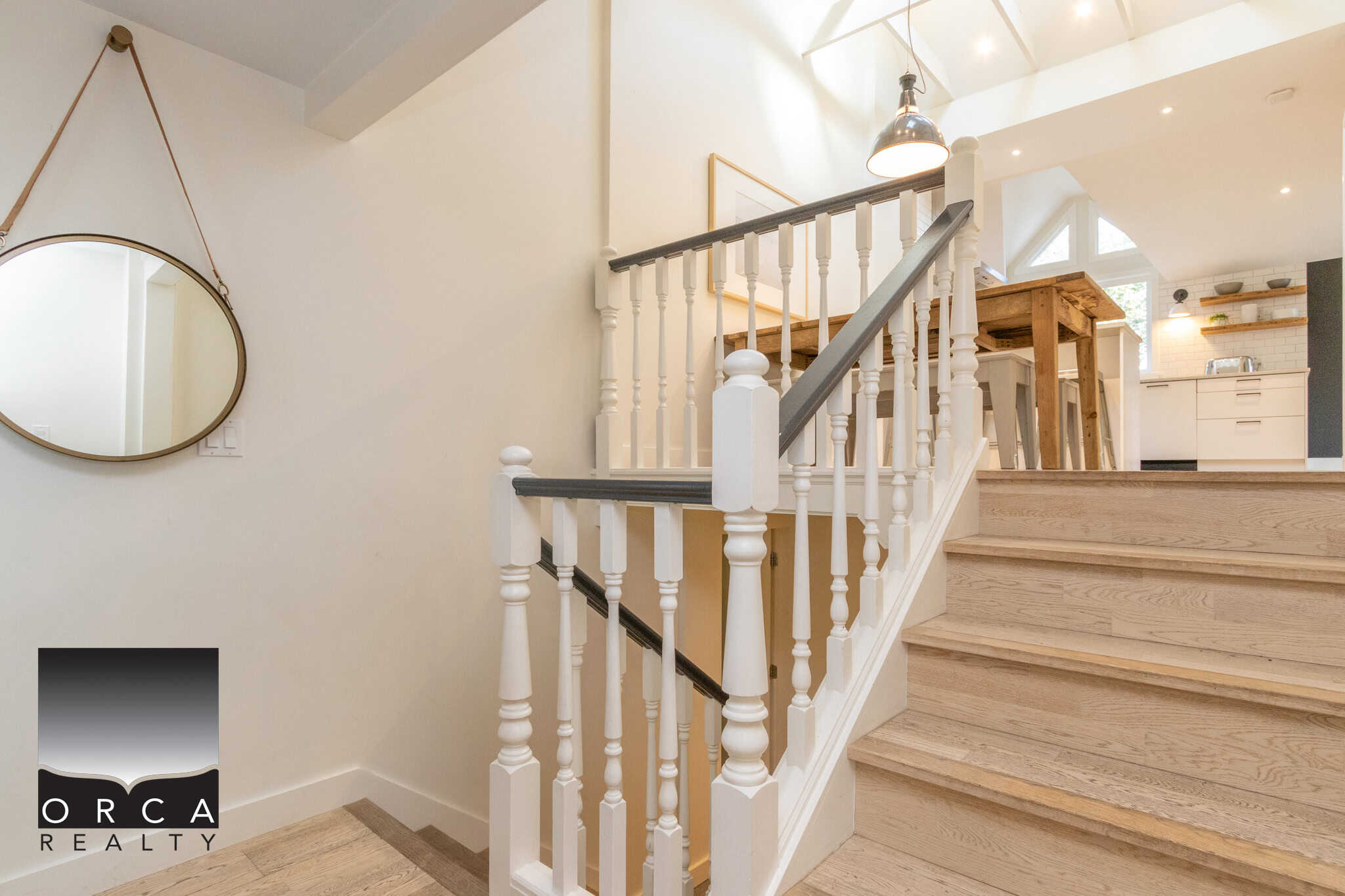 20 Bright modern staircase in a stylish home with wooden flooring and white railings, featuring contemporary decor and open-plan kitchen area, showcasing Orca Realty Inc. services in real estate listing.