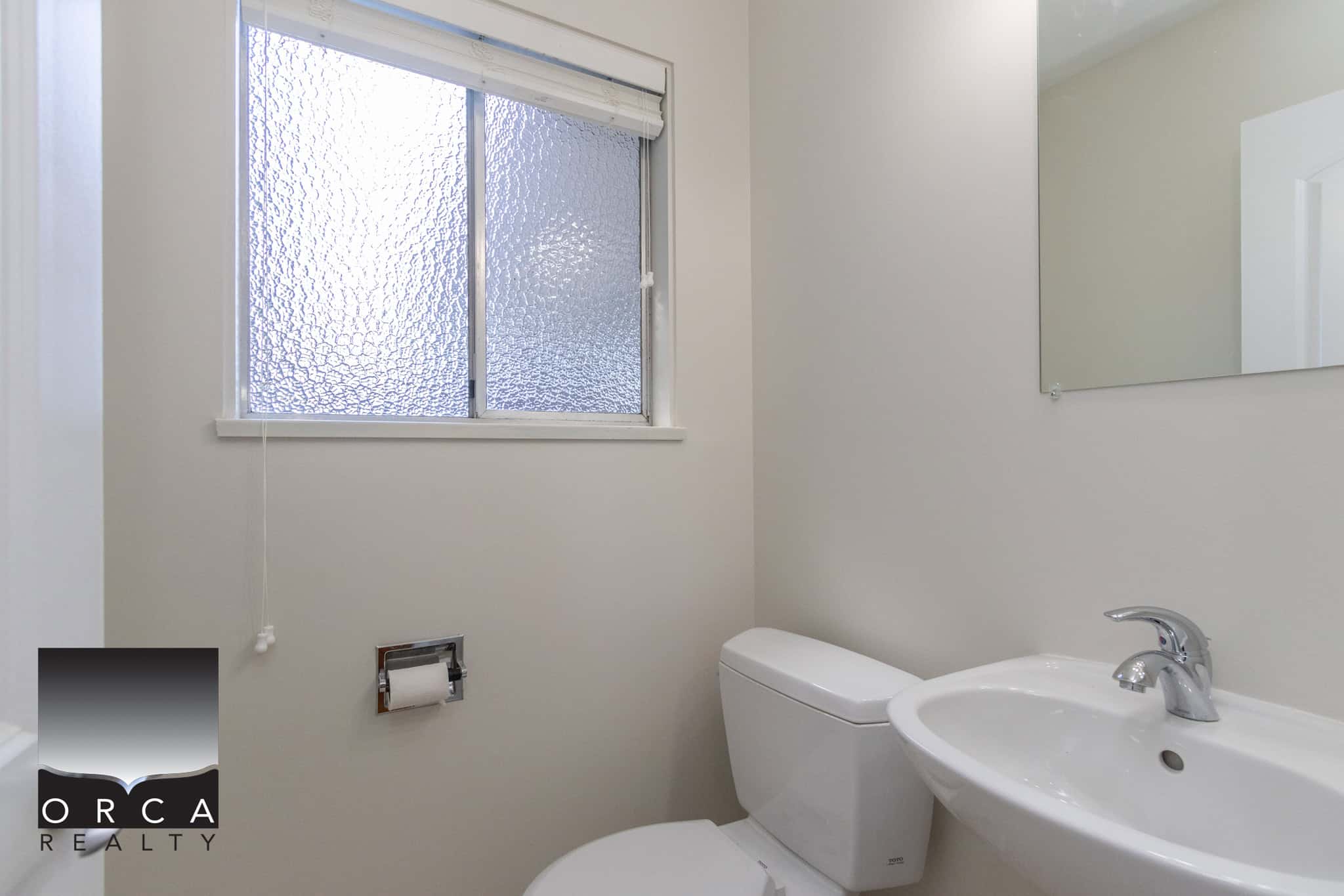 Bright bathroom with frosted window, white toilet, sink, and minimalist design, ideal for Vancouver homes; contact Orca Realty Inc. for Vancouver real estate services.