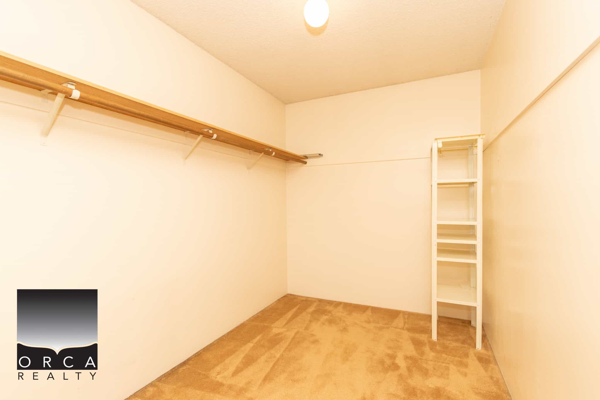 Spacious walk-in closet with beige carpeting, wooden shelves and hanging rods, ideal for organizing clothing and accessories, part of a modern home or apartment listing.