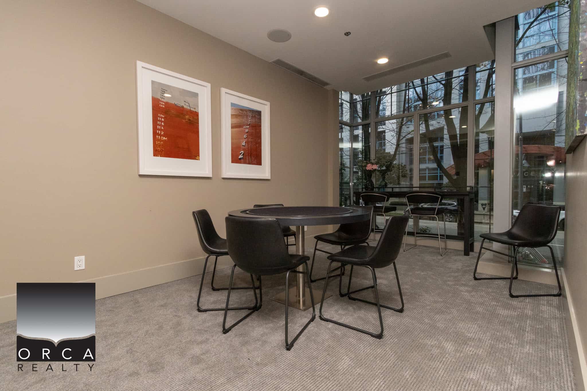 Modern interior of Orca Realty Inc. office with a round poker table, black chairs, large windows, and contemporary artwork, creating a professional and inviting environment for clients.