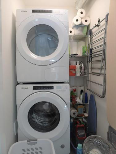 Front-loading washing machine and dryer in a compact laundry room with cleaning supplies and storage shelves, highlighting efficient household appliances and organization.