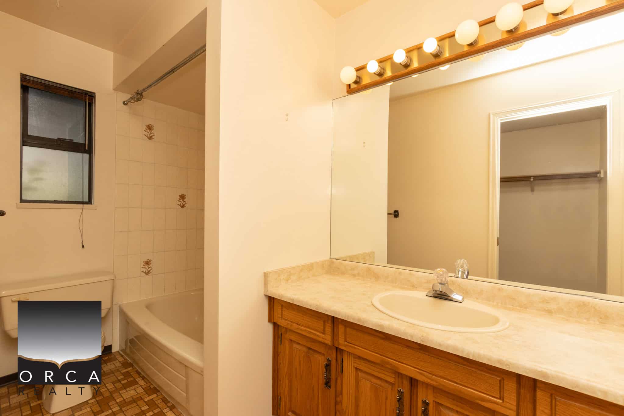 Bright bathroom with wooden vanity, large mirror, vintage lighting, bathtub, and small window, perfect for comfortable home living.