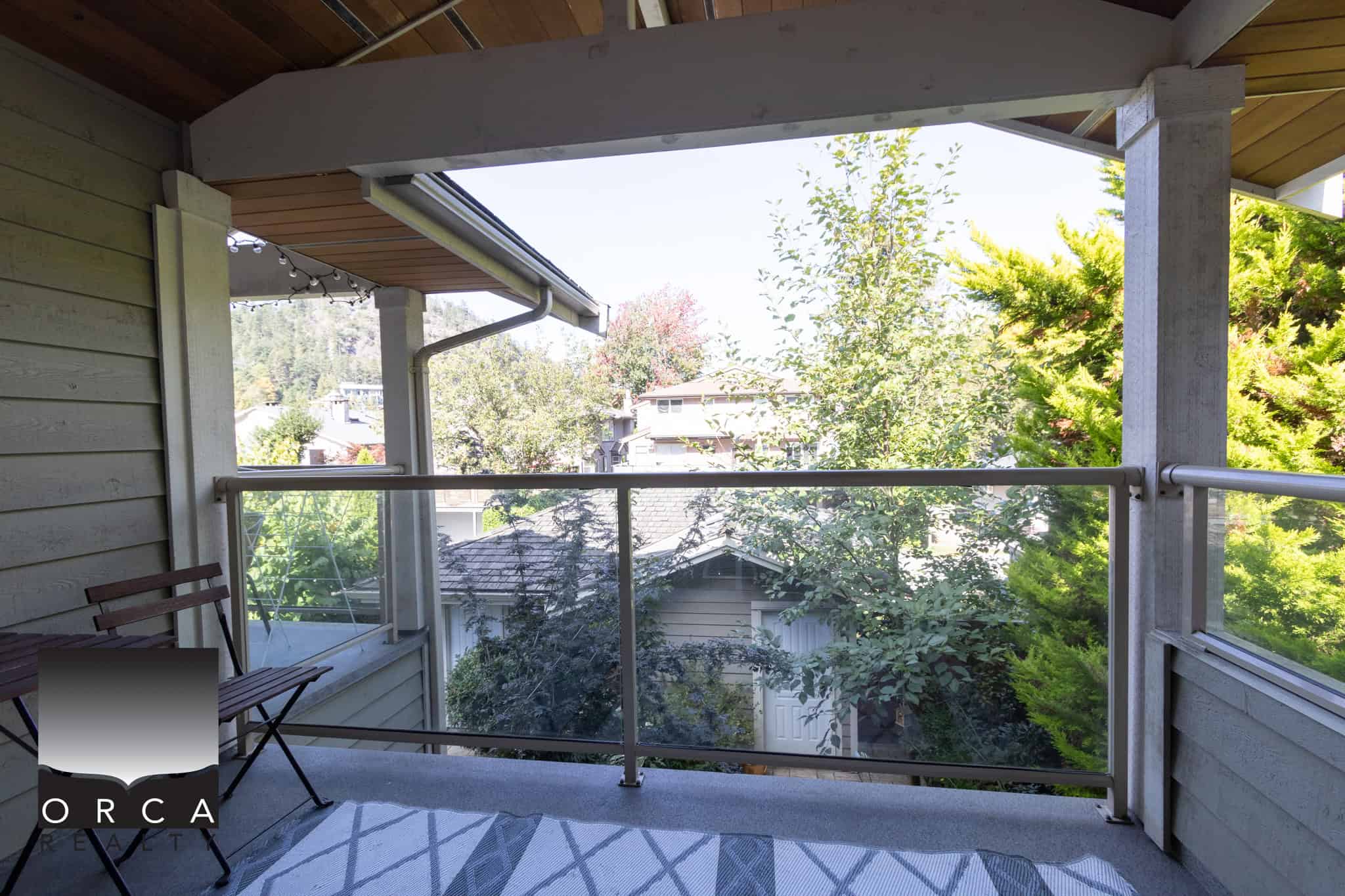 22 Spacious balcony with glass railing overlooking lush greenery and neighboring houses, perfect for outdoor relaxation and enjoying Vancouver’s natural beauty.