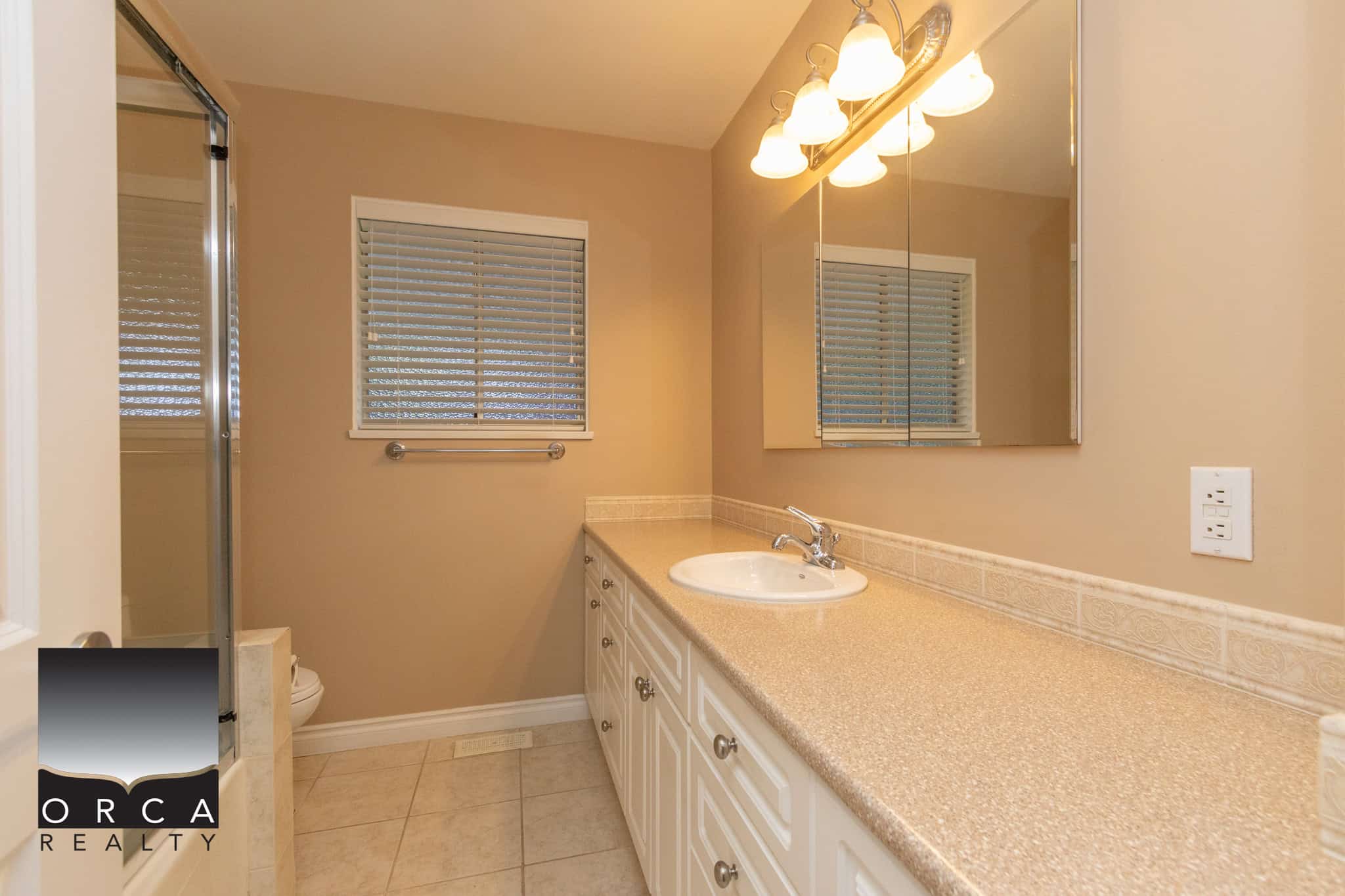 Spacious beige bathroom with a large vanity, white cabinetry, and a mirror, featuring modern lighting fixtures. Perfect for real estate listings emphasizing home interior and bathroom features in BC.
