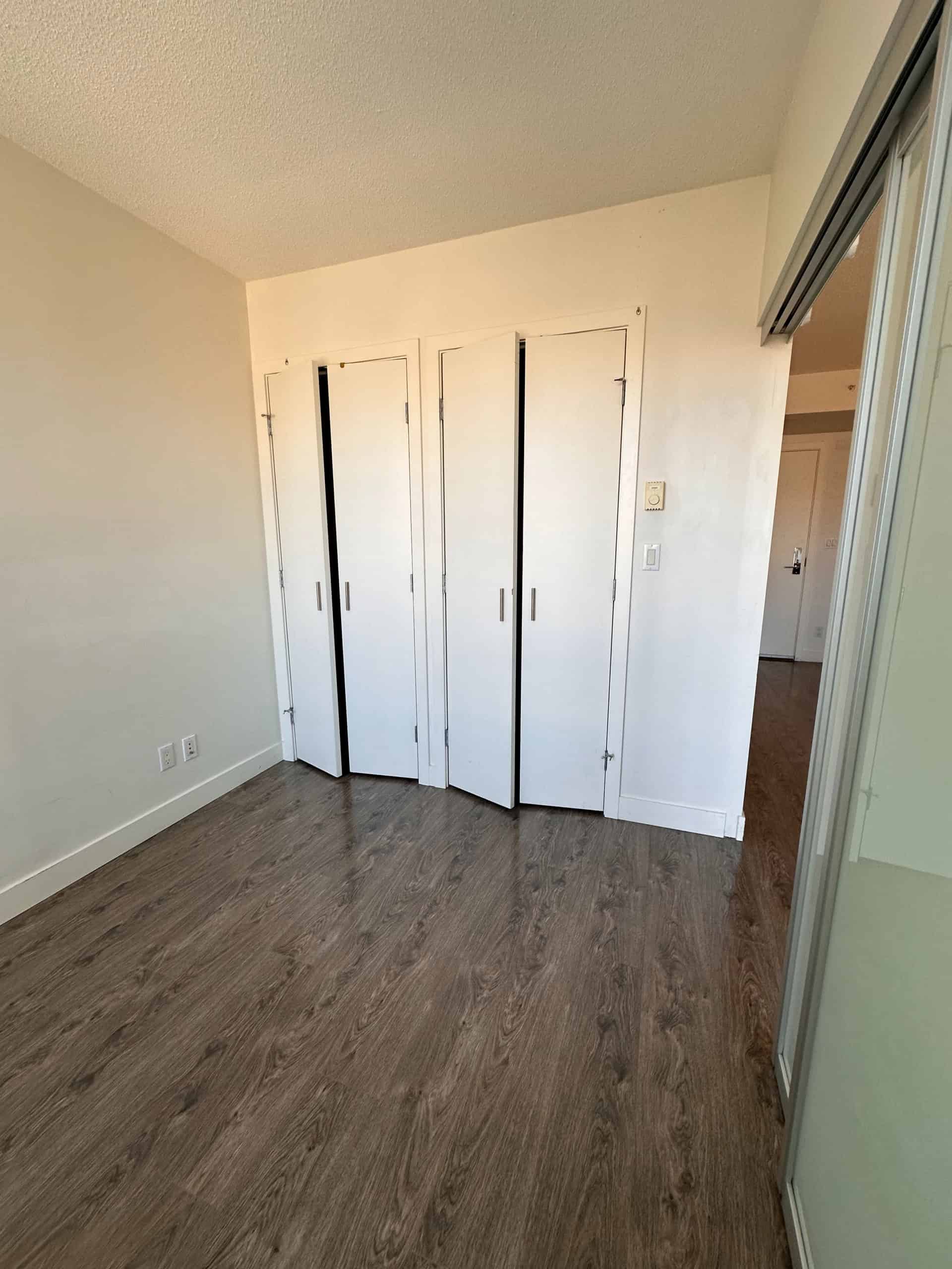 Bright modern bedroom with white walls, wood flooring, and built-in closet with folding doors; ideal Vancouver real estate offering.
