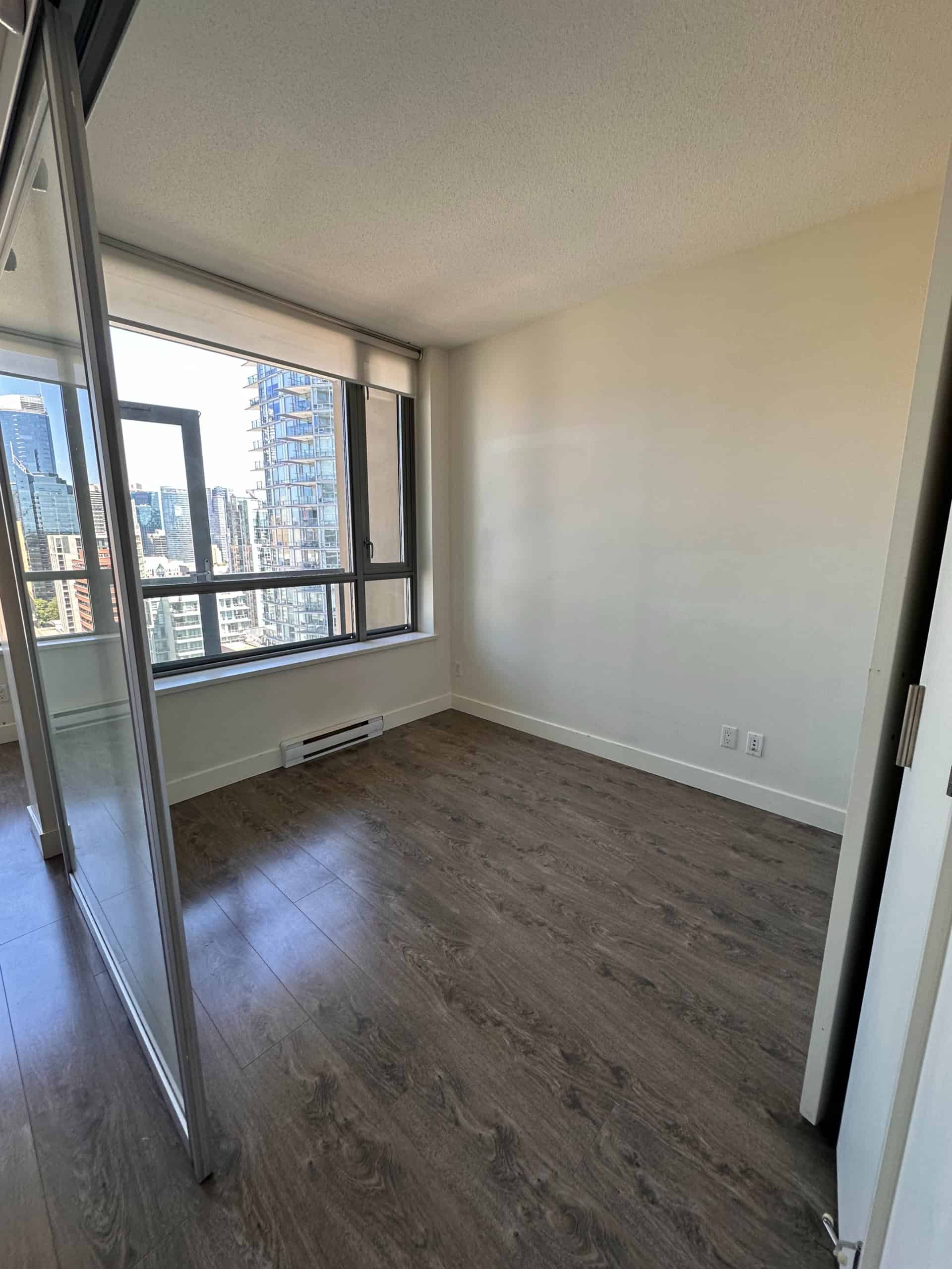 Contemporary city-view bedroom in Vancouver high-rise, featuring large windows, hardwood floors, and modern decor, ideal for urban living with access to downtown amenities.