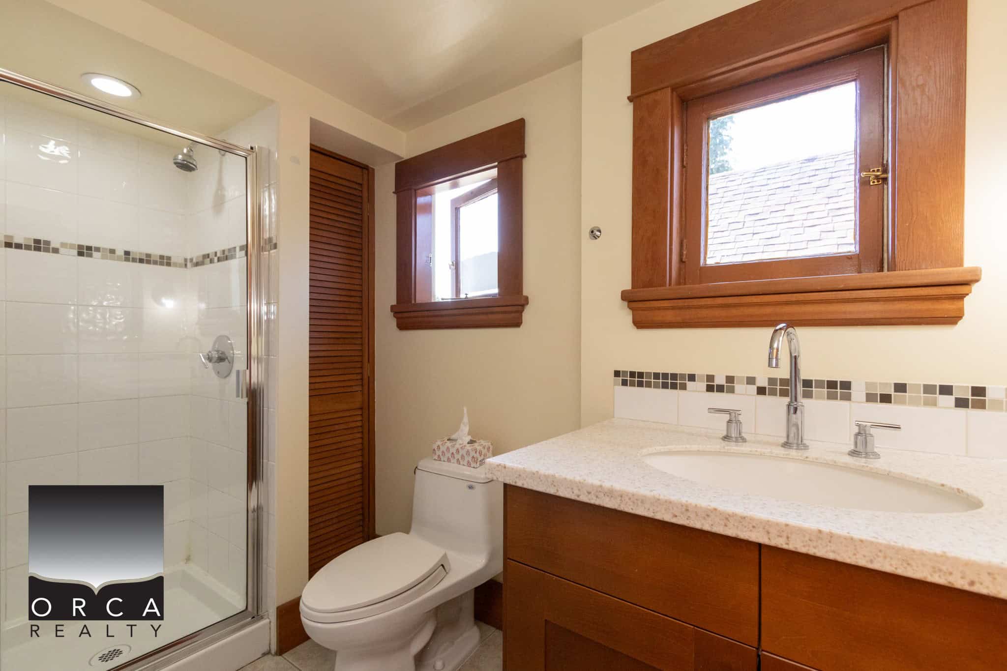 Modern bathroom featuring a glass-enclosed shower, wooden window frames, and a contemporary vanity with a granite countertop, perfect for coastal home living.