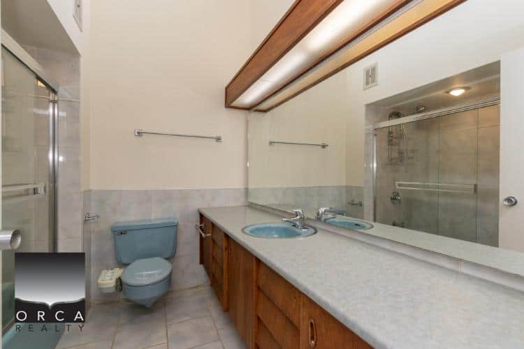 Bright bathroom with dual sinks, wooden cabinetry, large mirror, modern shower, and neutral tiles, ideal for Vancouver real estate listings.