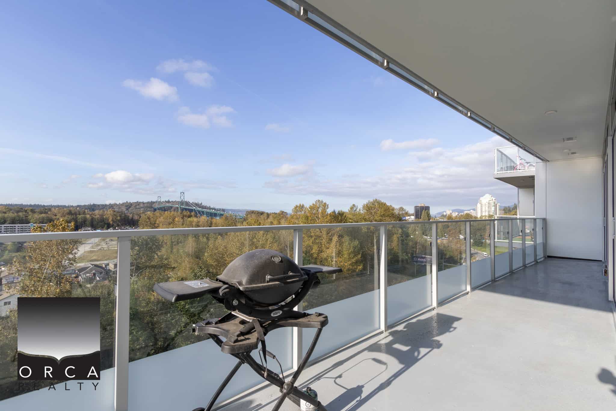 Spacious balcony with modern glass railing offering panoramic city and forest views, ideal for outdoor living and relaxation in Vancouver's real estate market.