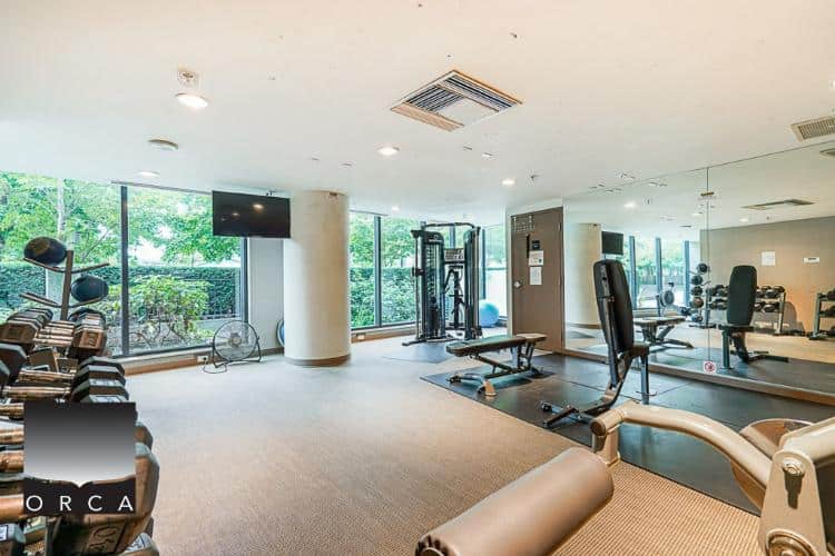 Modern gym and fitness centre at Orca Realty Inc. featuring cardio equipment, weight machines, and free weights with large windows and natural lighting, ideal for health-conscious clients.