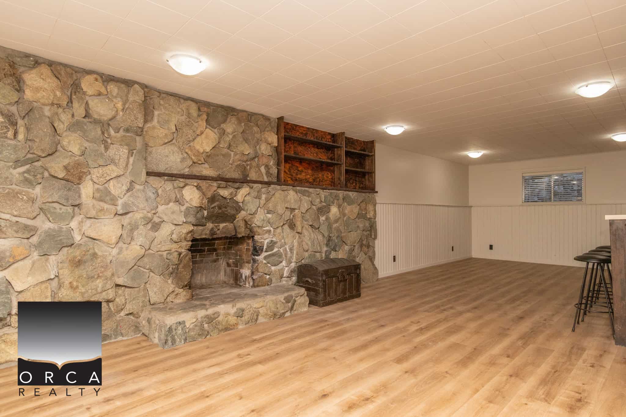Cozy finished basement with a rustic stone fireplace and elegant wood accents, Ideal for entertaining or relaxing, located in a desirable neighbourhood in En CA.