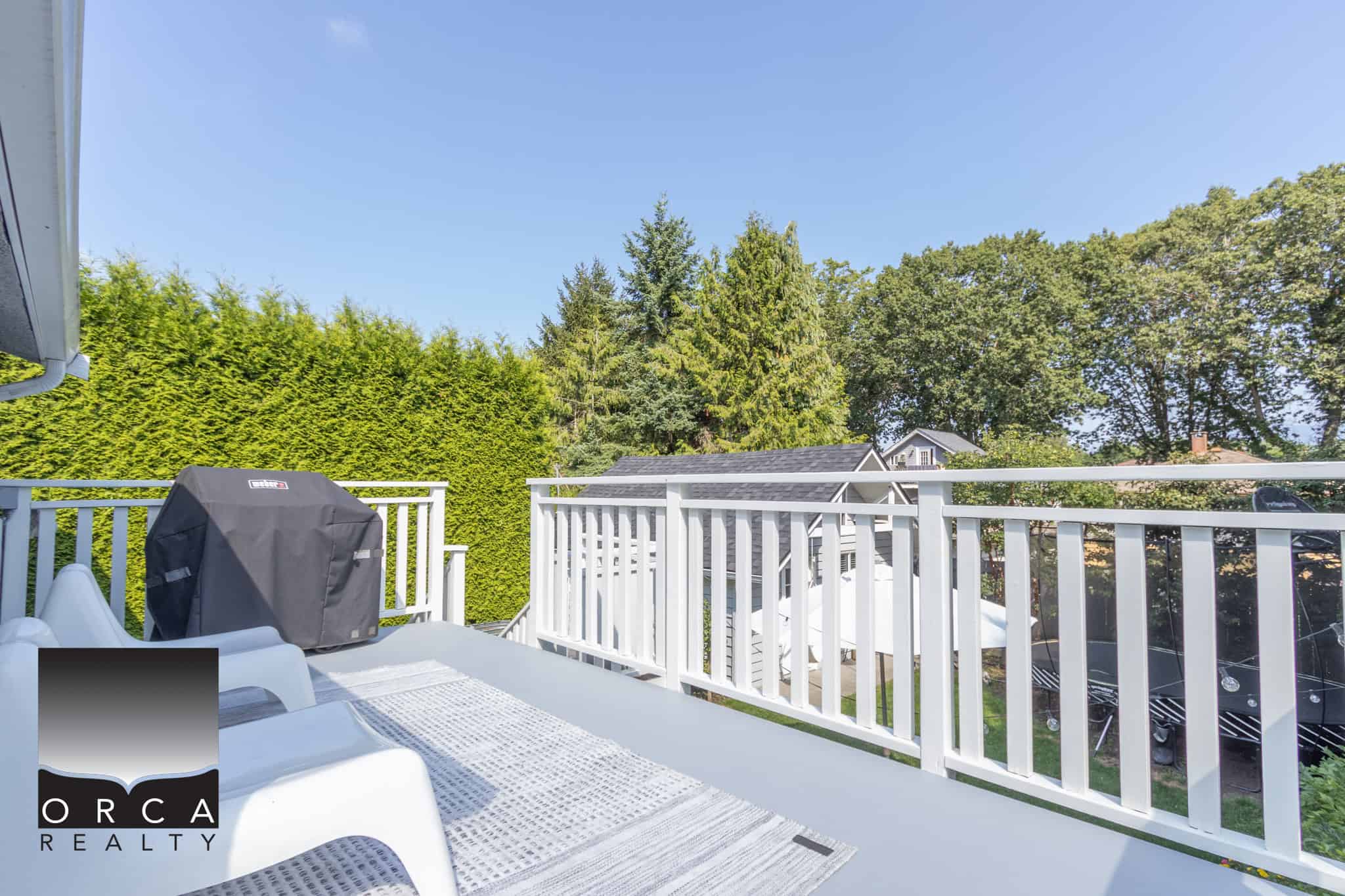 25 Bright outdoor balcony with white railing, outdoor furniture, and a barbecue, surrounded by lush green trees and neighboring houses, perfect for relaxing and enjoying Vancouver Island's nature.