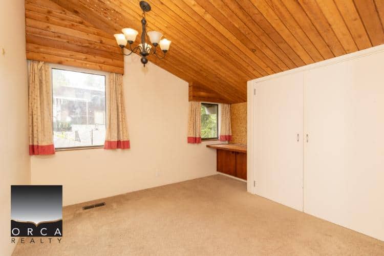 Spacious interior room with vaulted wooden ceiling, natural light from windows, featuring classic curtains and built-in storage, ideal for comfortable home living in Vancouver.