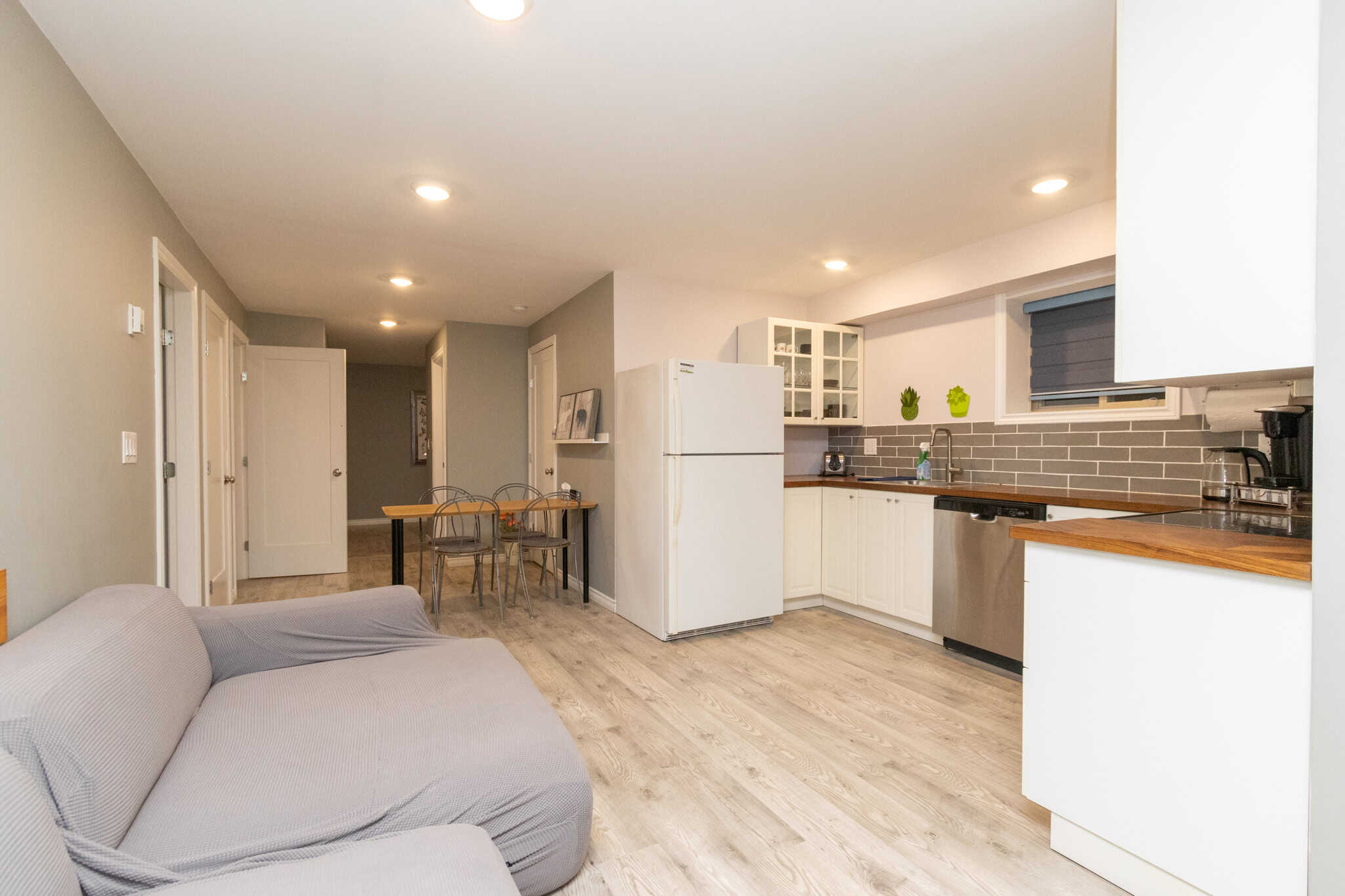 25 Modern open-concept kitchen and living space in a Vancouver-area home, featuring white cabinetry, wooden countertops, and a cozy grey sofa for comfortable living.
