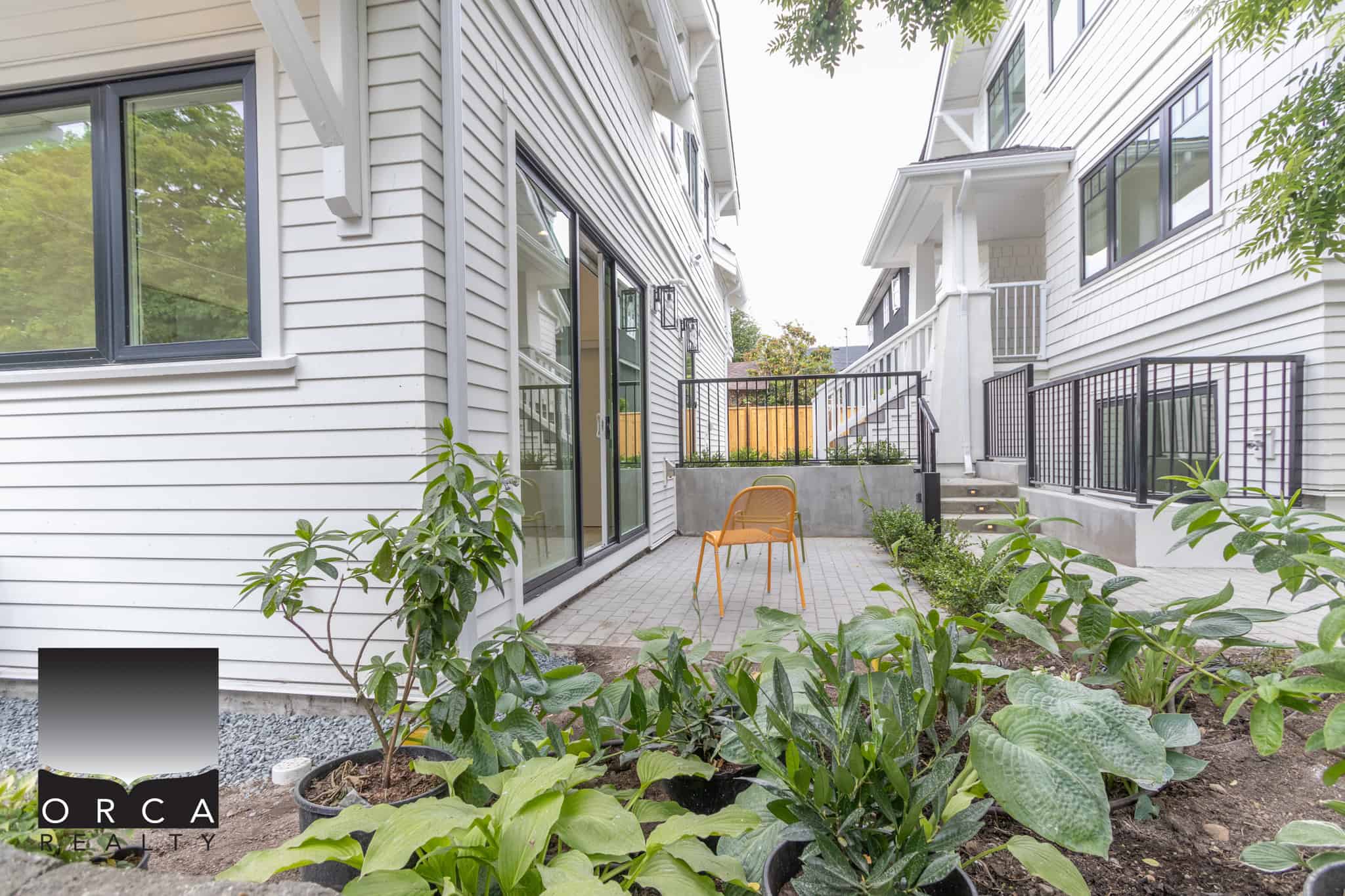Modern outdoor patio area with potted plants, garden space, and adjoining homes, ideal for Vancouver Island real estate or duplex/strata property listings.