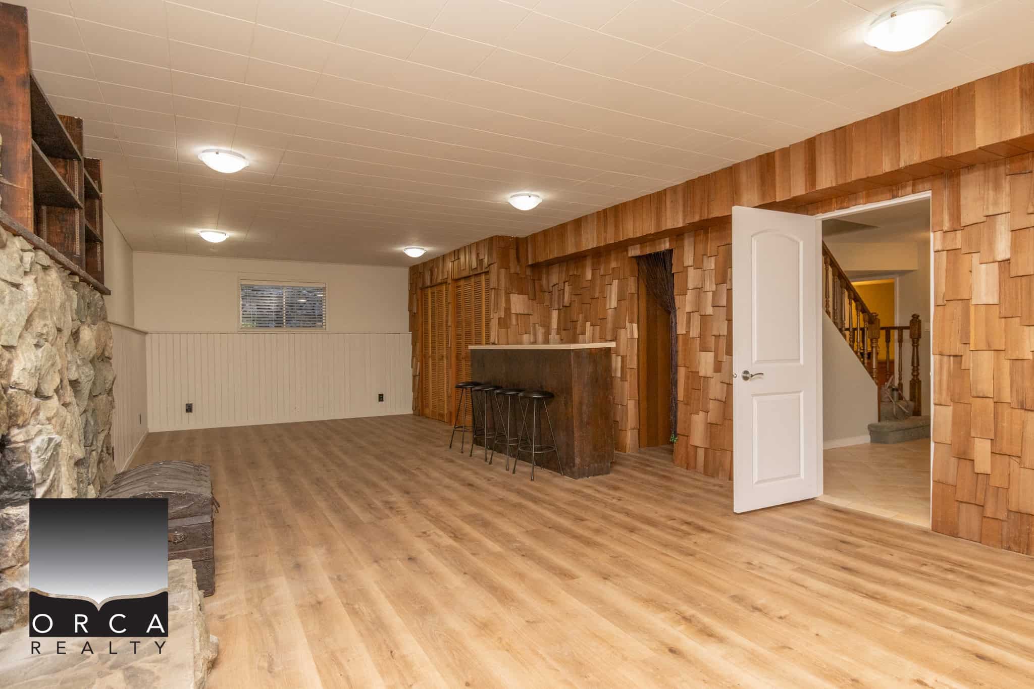 Spacious basement living area featuring warm wood flooring, textured wood accent walls, and ample lighting, ideal for family gatherings or entertainment spaces in a Vancouver-area home.