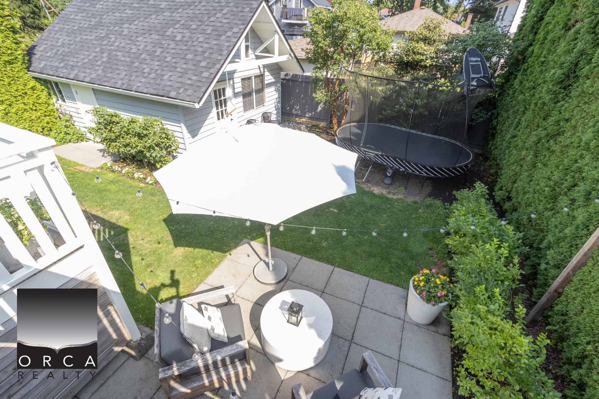 26 Aerial view of a cozy backyard featuring a trampoline, patio seating with an umbrella, lush green lawn, flowering plants, and a small shed, showcasing ideal outdoor living space in Vancouver.