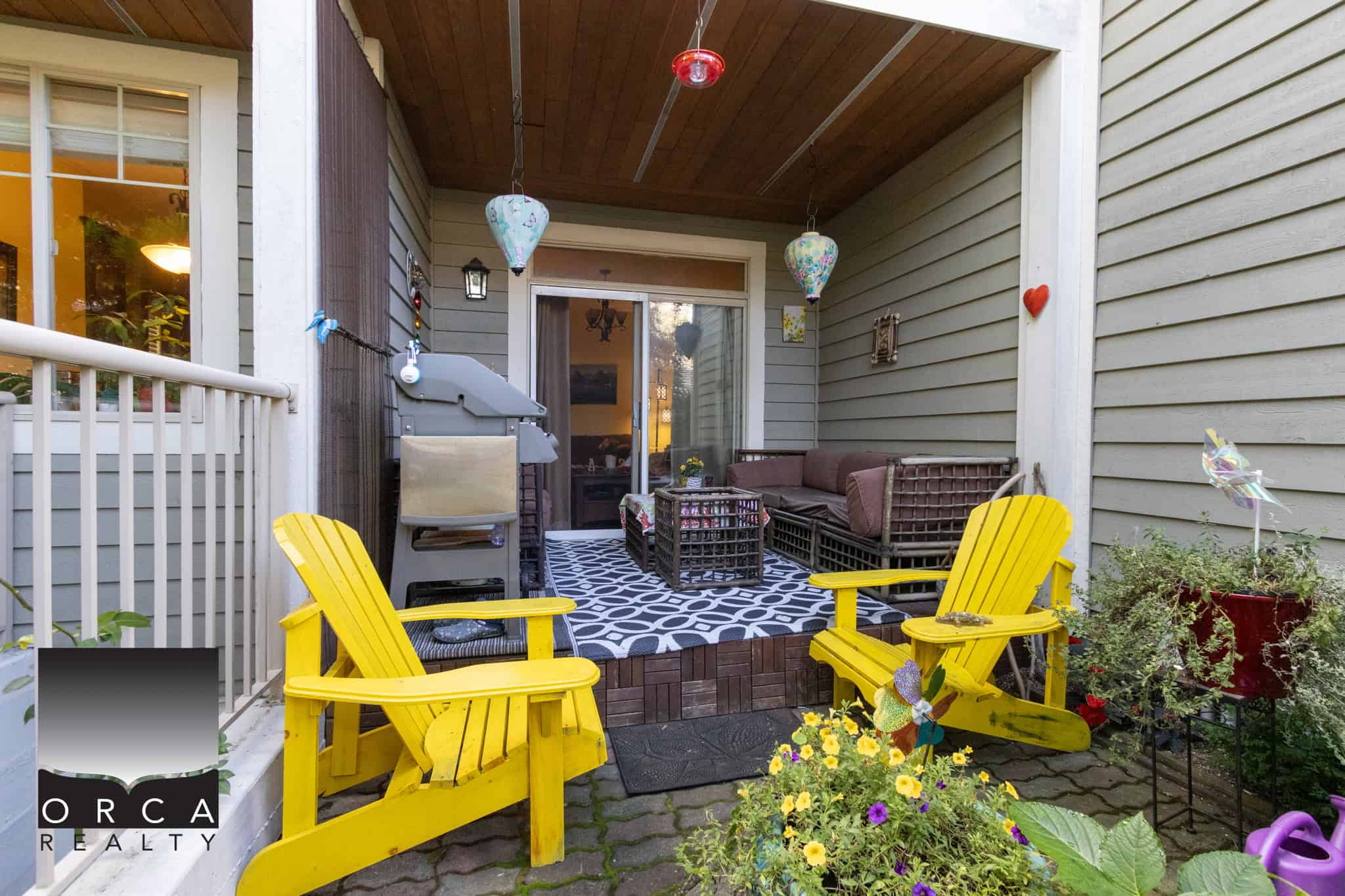 26 Cozy backyard patio with vibrant yellow Adirondack chairs, decorative hanging lanterns, lush potted plants, and a comfortable seating area, perfect for outdoor living and entertaining.