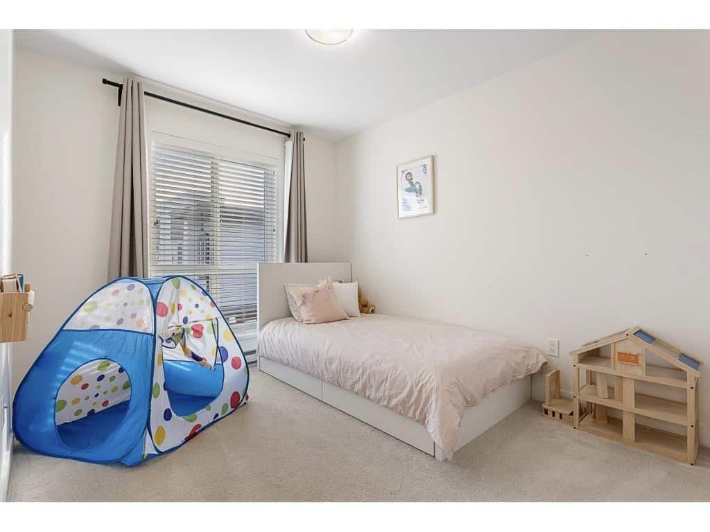 Bright bedroom with a child's play tent, featuring a modern white bed, natural light from large window with beige curtains, and minimal decor in a family-friendly home.