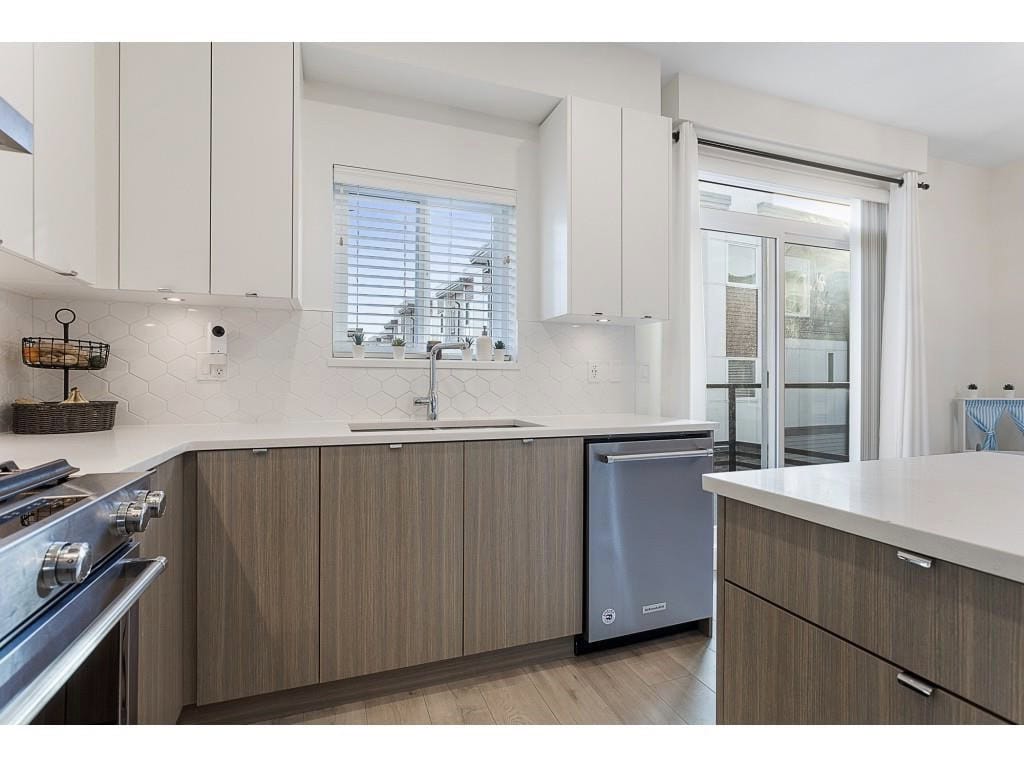 Bright modern kitchen with white cabinetry, stainless steel appliances, and ample natural light in a contemporary condo. Features a spacious island, large window, and outdoor access.