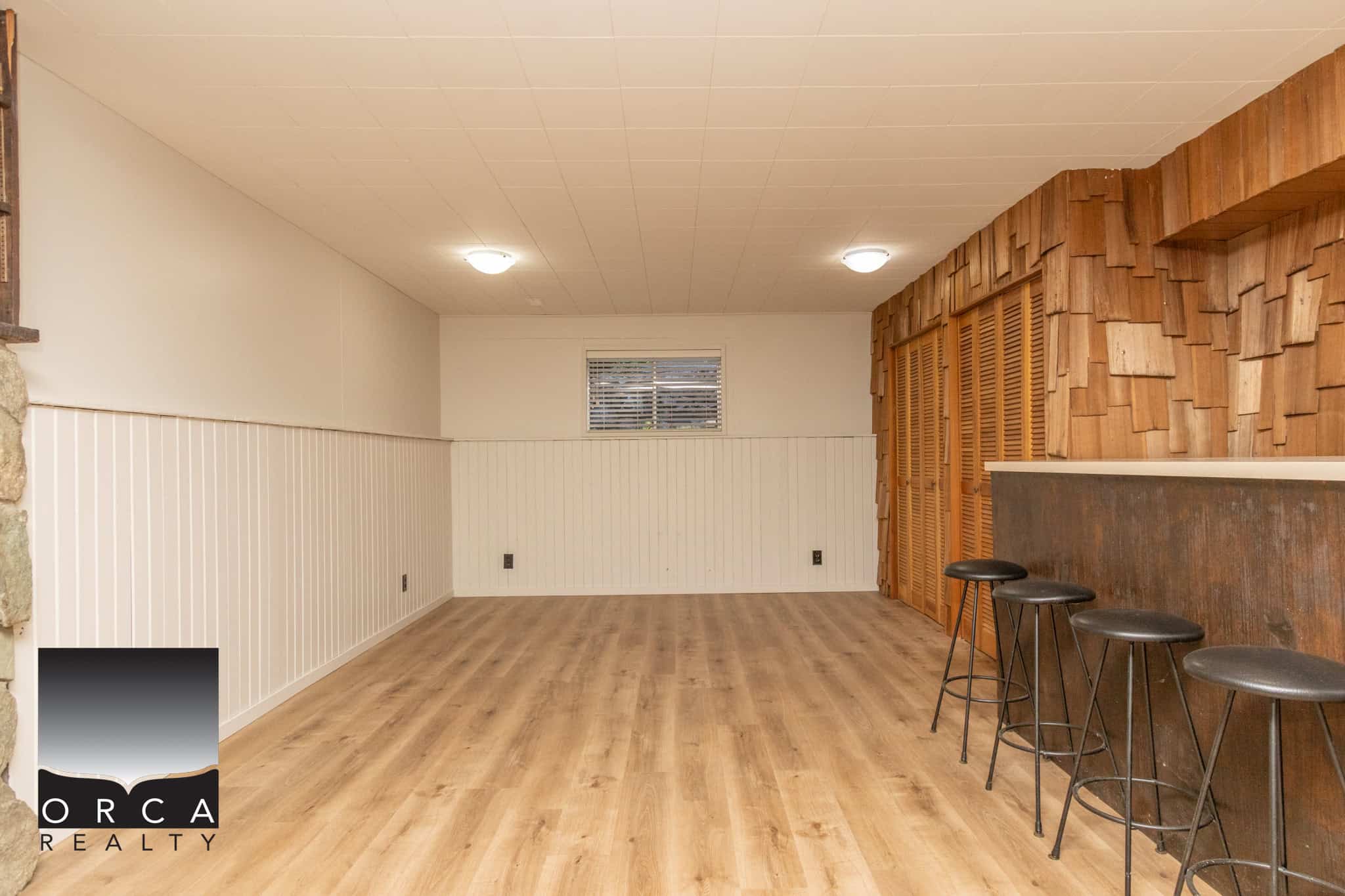 Bright basement space featuring wooden accents and bar stools, perfect for entertaining, with smooth flooring, white wainscoting, and a cozy window providing natural light.