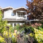 Lush garden with vibrant greenery and flowering plants surrounds a modern two-story home in Vancouver, BC, showcasing desirable real estate options by Orca Realty Inc.