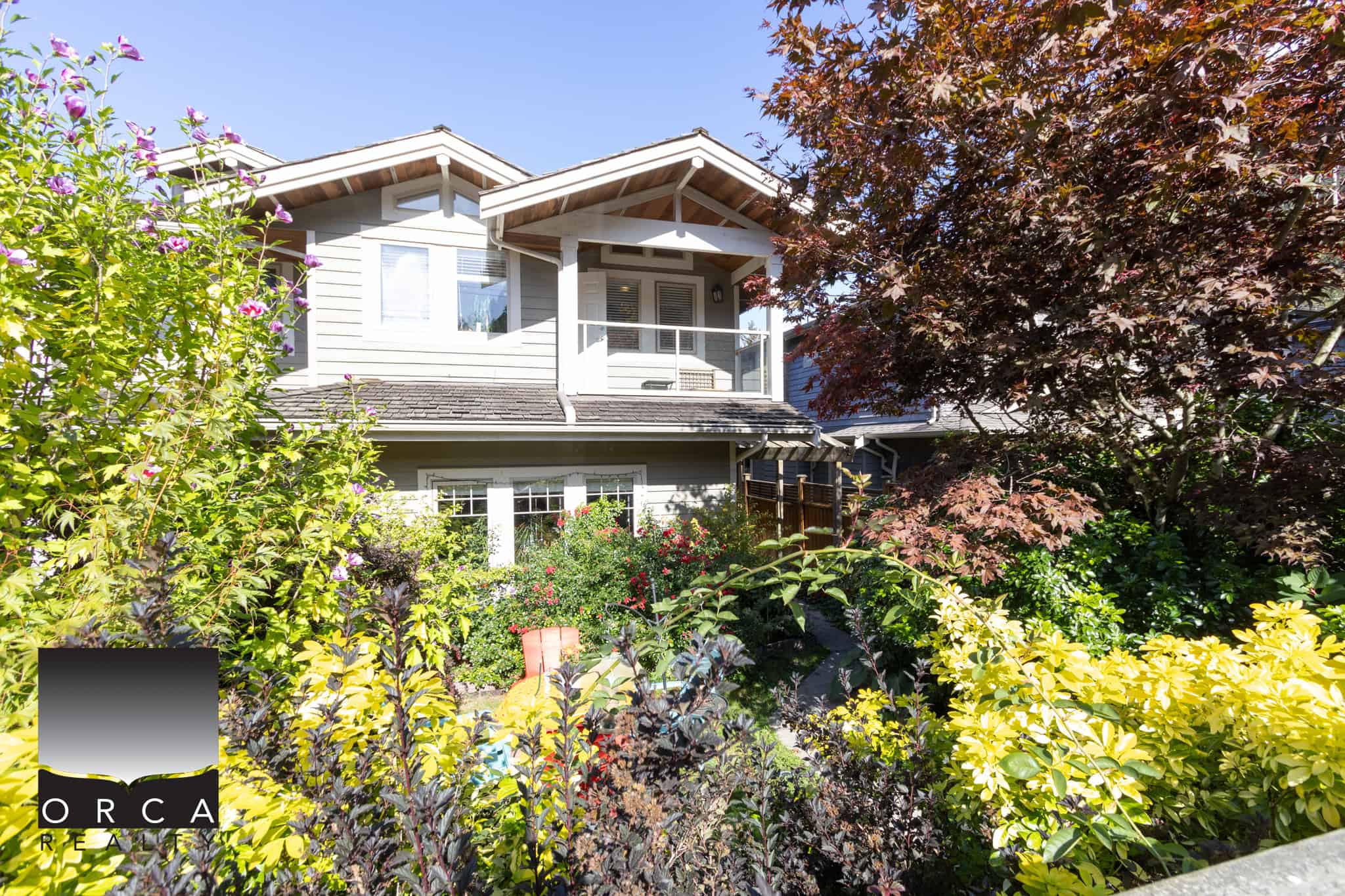 27 Lush garden with vibrant greenery and flowering plants surrounds a modern two-story home in Vancouver, BC, showcasing desirable real estate options by Orca Realty Inc.