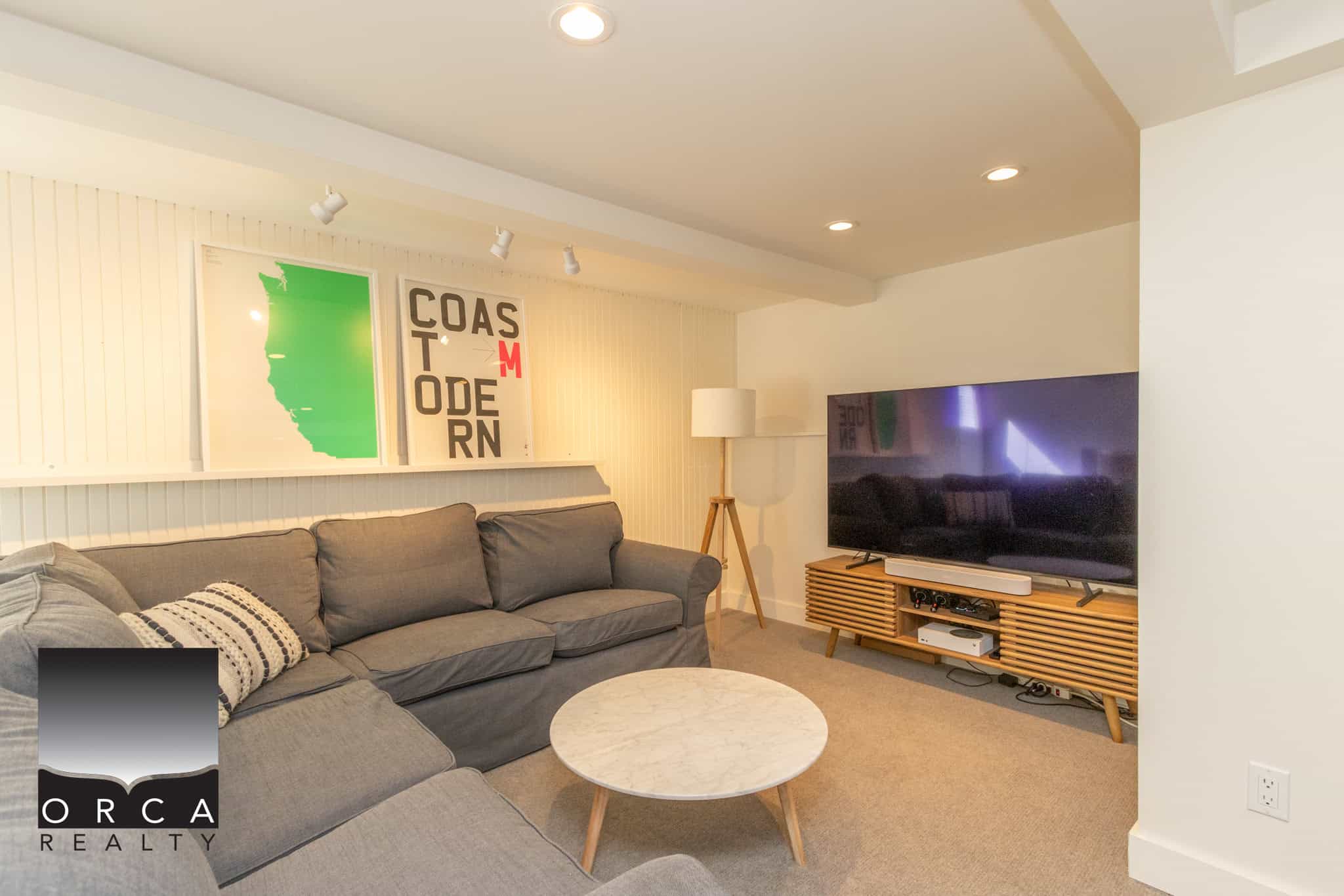 28 Modern living room with grey sofa, wall art of California and Oregon map, flat-screen TV, wooden media console, cozy lamp, and neutral tones, perfect for Vancouver Island real estate.