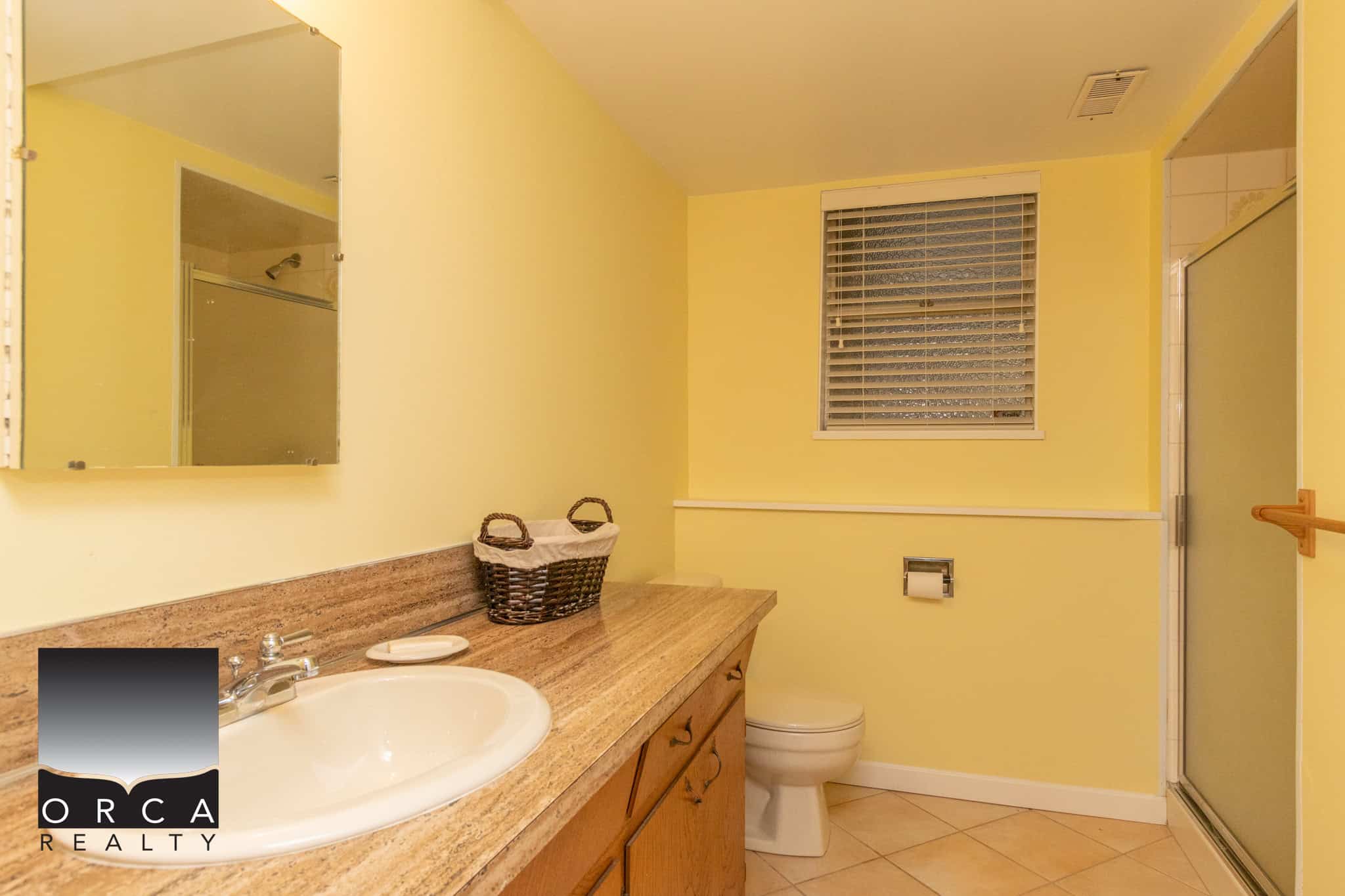 Bright yellow bathroom interior featuring a single sink vanity with a granite countertop, a mirror, a window with blinds, and a walk-in shower, showcasing a welcoming and functional space for homeowners.