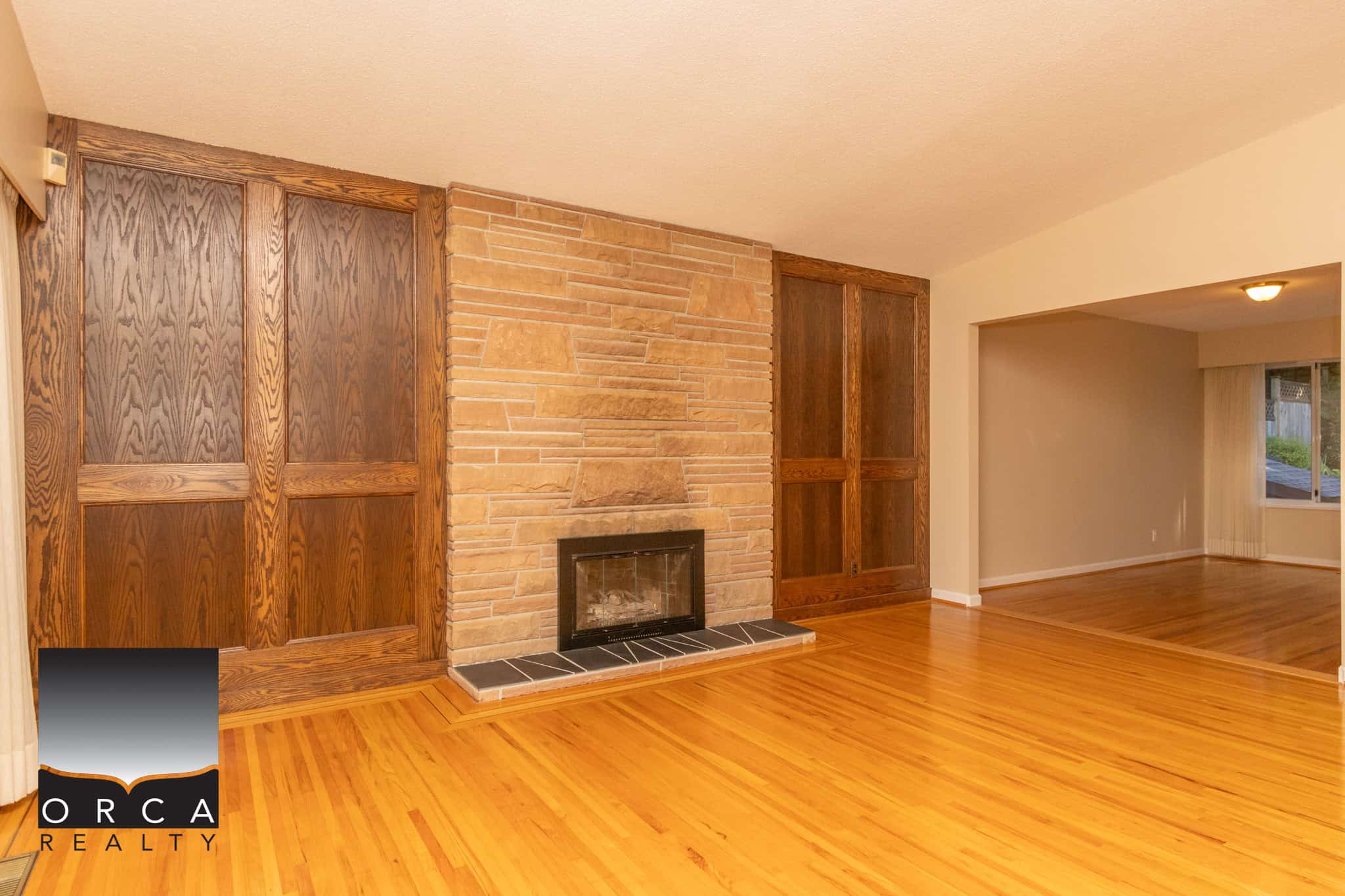 Spacious living room with a cozy fireplace, wood paneling, and hardwood floors in a Vancouver home listed by Orca Realty Inc.