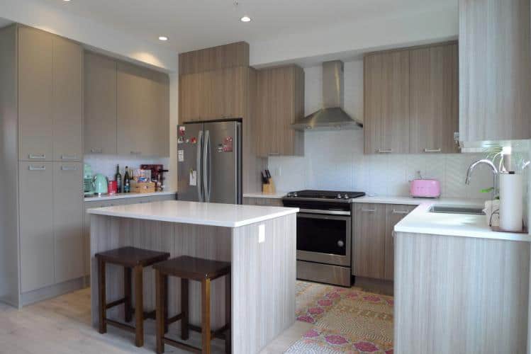 Modern kitchen with light wood cabinets, stainless steel appliances, and a white island, perfect for homebuyers seeking contemporary Vancouver Island real estate.