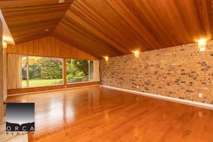 Bright spacious living room with large window, hardwood floors, exposed brick wall, and vaulted wood ceiling, perfect for Vancouver real estate and home staging in BC.