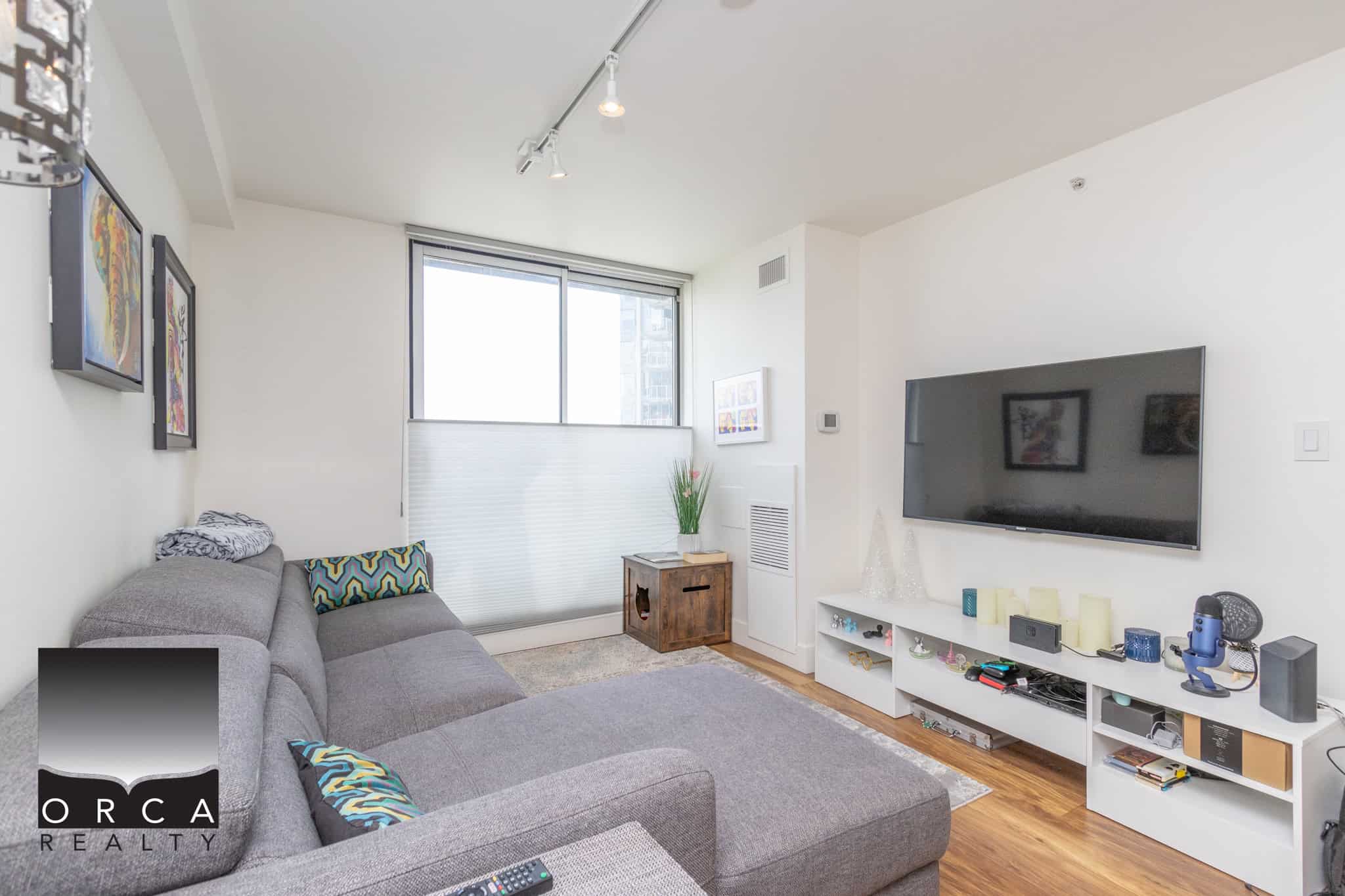 3 Modern Vancouver condo living room featuring a comfortable grey sectional, flat-screen TV, stylish decor, and hardwood floors, perfectly showcasing Orca Realty Inc.'s expertise in Vancouver real estate.