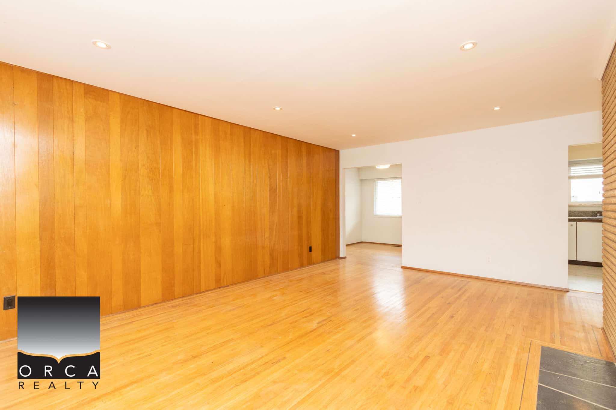 3 Spacious living room with hardwood flooring and warm wood-paneled accent wall, ideal for family gatherings and entertaining in Victoria BC.