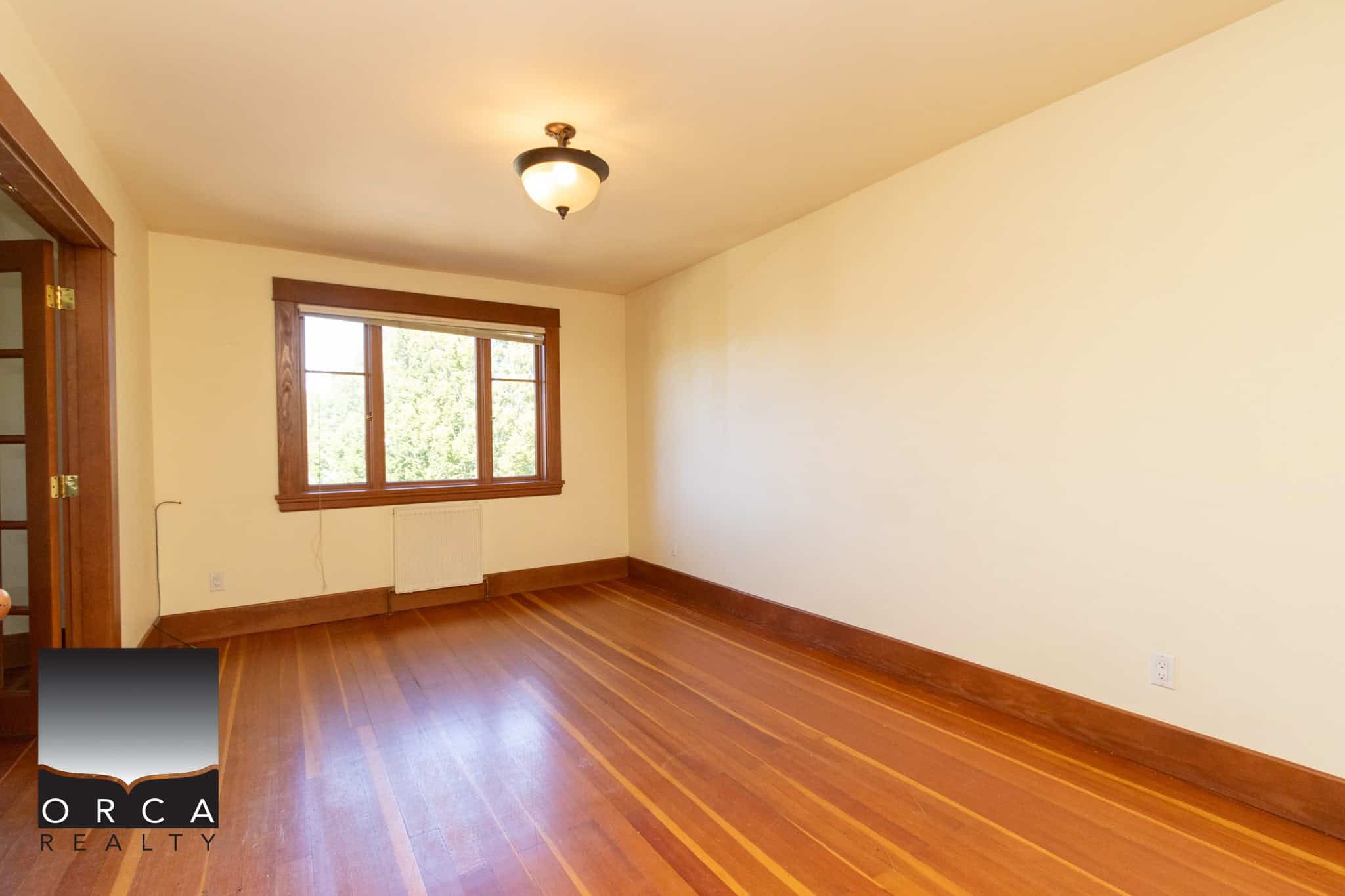 Bright empty living room with hardwood floors and large window, perfect for homebuyers seeking Vancouver Island real estate through Orca Realty Inc.