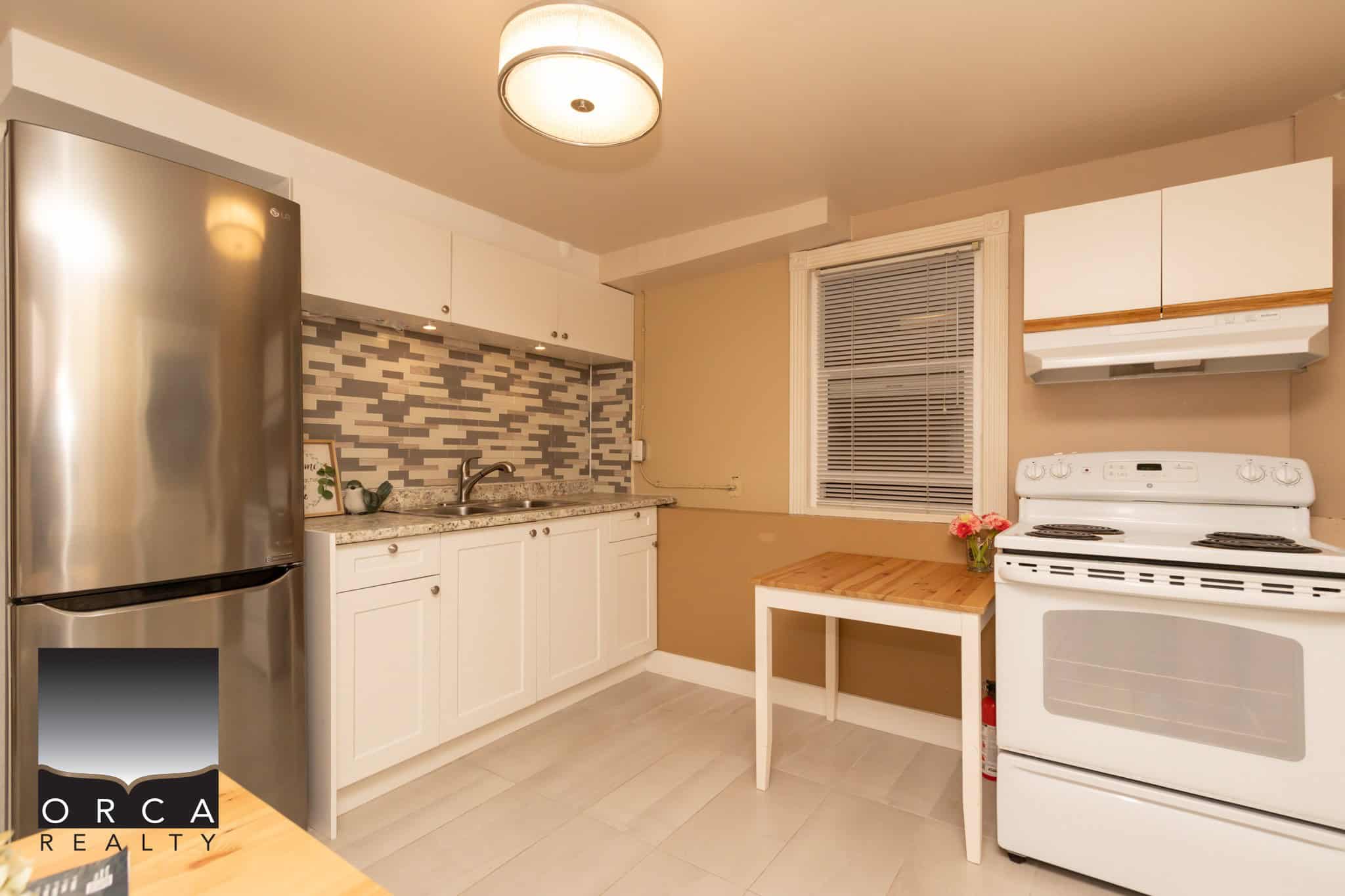 Modern kitchen with stainless steel fridge, white cabinetry, stylish backsplash, and cozy window, ideal for Vancouver Island real estate listings.