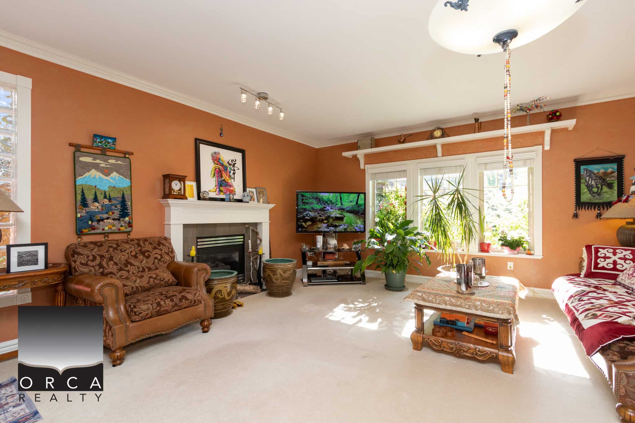 3 Spacious living room with warm orange walls, cozy fireplace, large window with natural light, and eclectic decor featuring plants and artwork, ideal for Vancouver Island real estate.