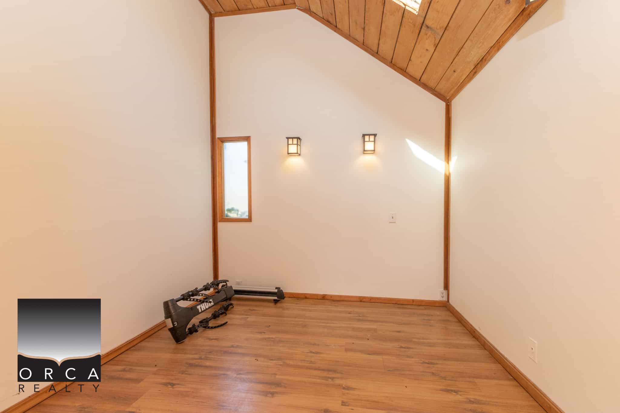 30 Flexible home office or bedroom with wood accents and natural light, featuring hardwood flooring, modern wall sconces, and a vaulted wooden ceiling. Perfect space for relaxed living or remote work.