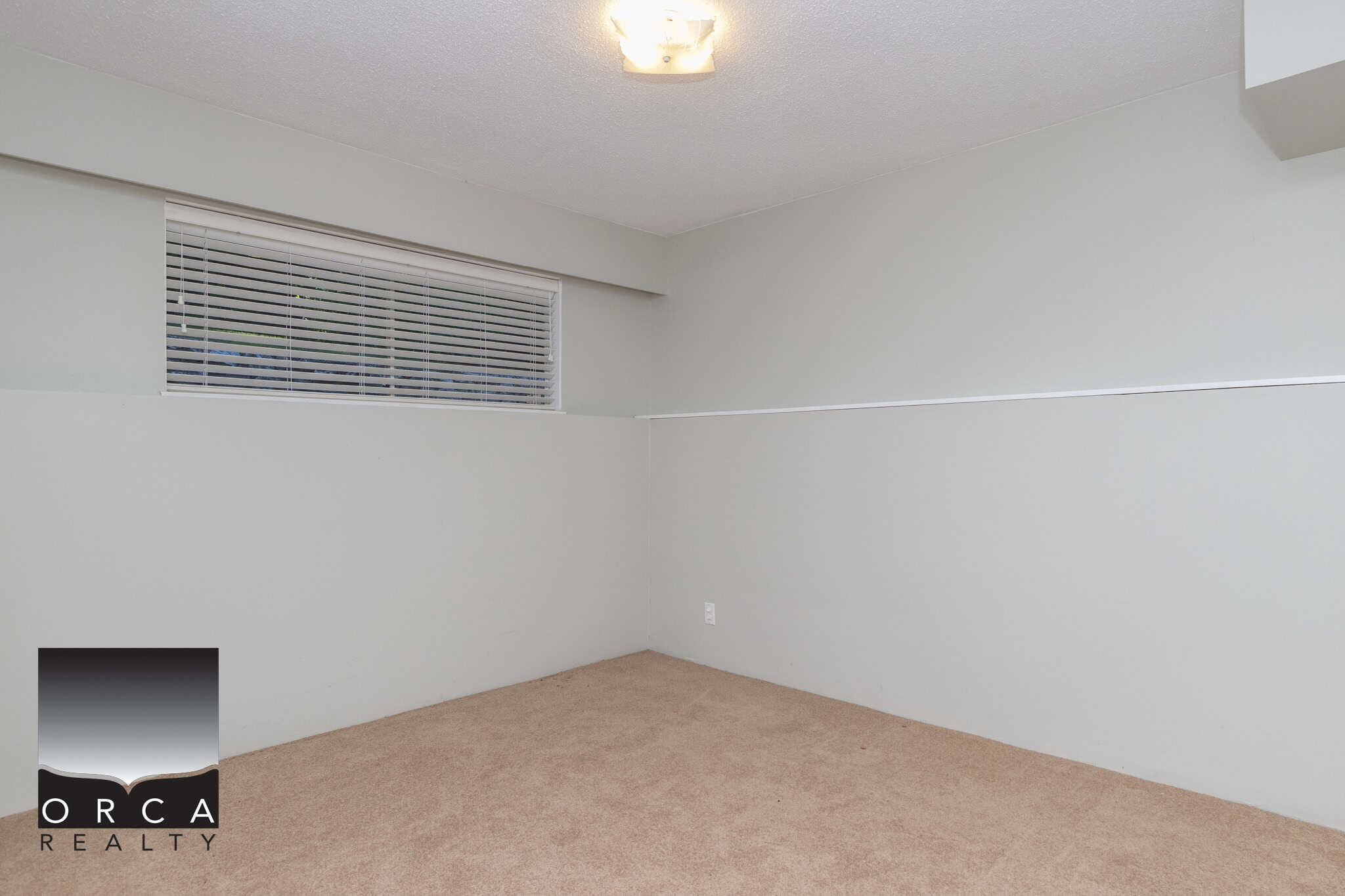 Clean, empty room with beige carpet, white walls, and a window with white blinds, showcasing the inviting interior of a property listed by Orca Realty Inc.
