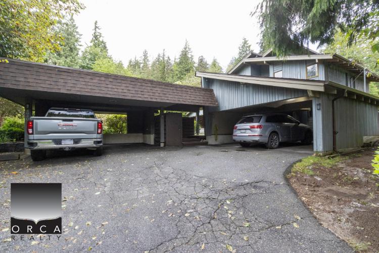 Spacious garage and parking area at a modern home by Orca Realty Inc., surrounded by lush greenery, ideal for property buyers seeking homes with ample parking space in a serene setting.