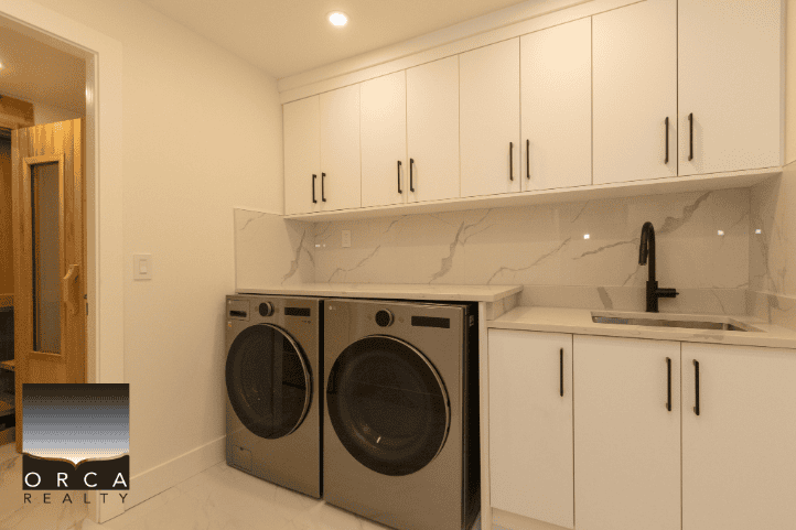 Washer and dryer in a modern laundry room with white cabinets and marble backsplash, part of Orca Realty Inc. property listing.