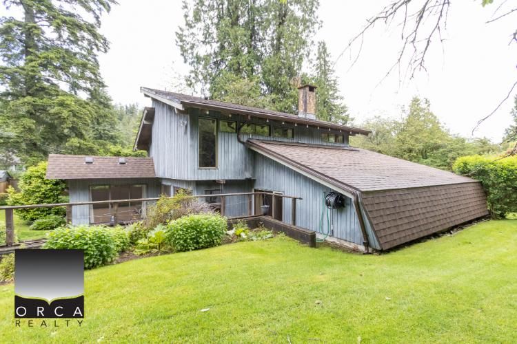 Cozy forest-style house with a sloped roof, surrounded by lush greenery and mature trees, perfect for nature lovers seeking a private retreat in British Columbia.